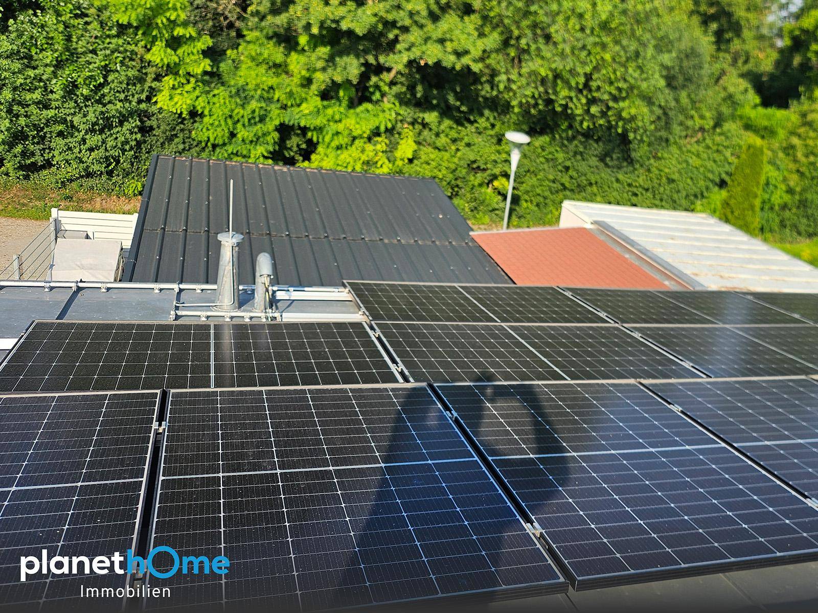 Solarmodule auf dem Dach eines Gebäudes mit grüner Umgebung und klarem Himmel.
