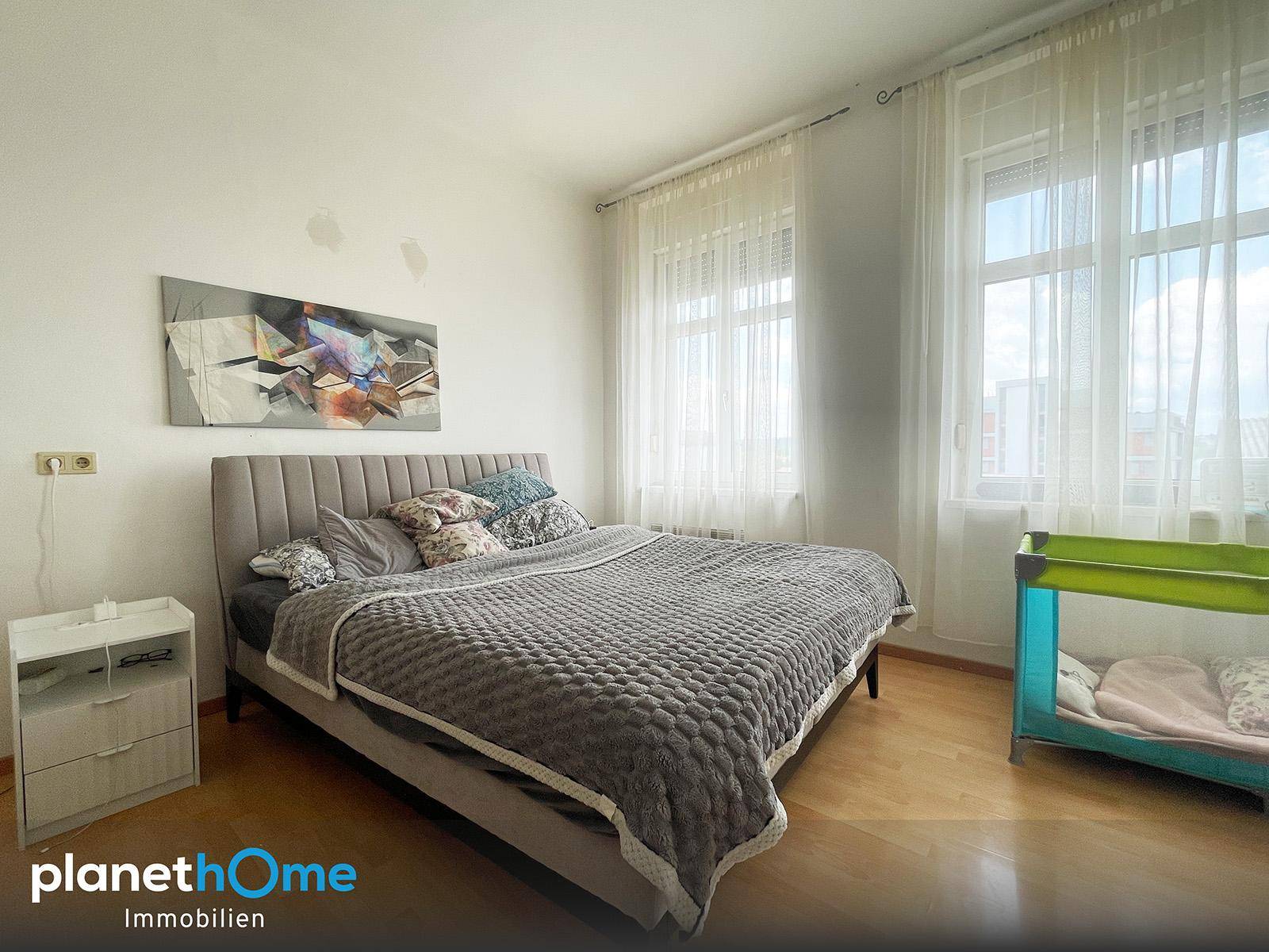 Helles Schlafzimmer mit großem Bett, zwei Fenstern und Holzfußboden, bietet viel Tageslicht.