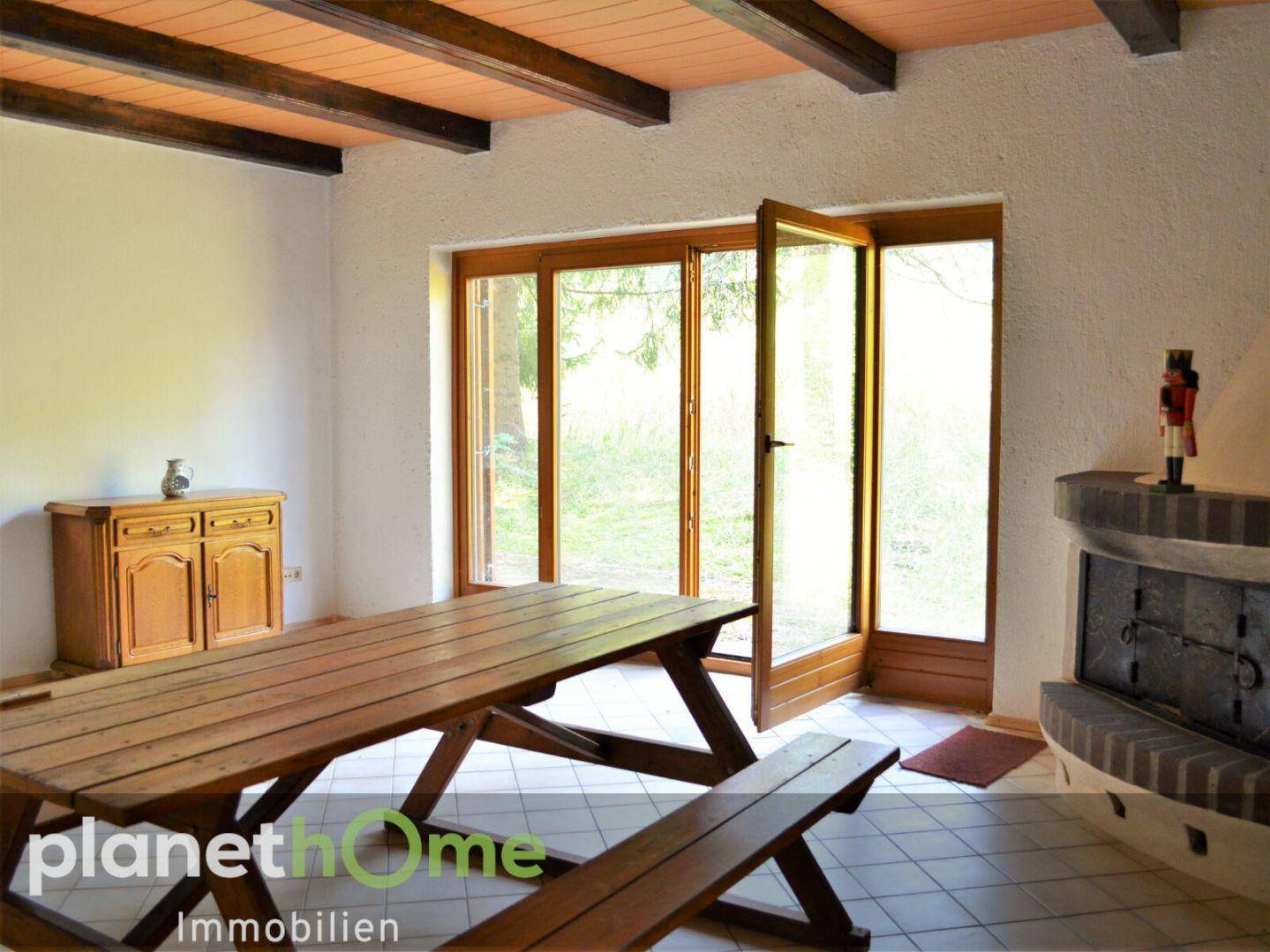 Rustikaler Innenraum mit großem Holztisch, Kamin und Zugang zur Natur durch Glastüren.