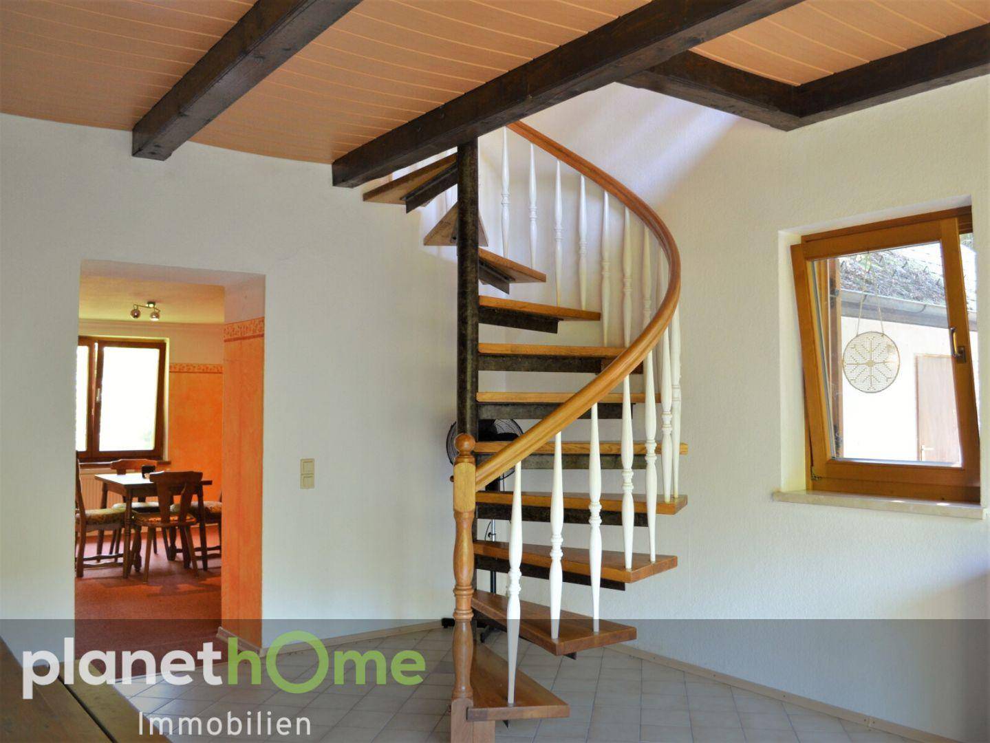 Geräumiger Flur mit eleganter Holzwendeltreppe, Fliesenboden und Blick in einen angrenzenden Raum.