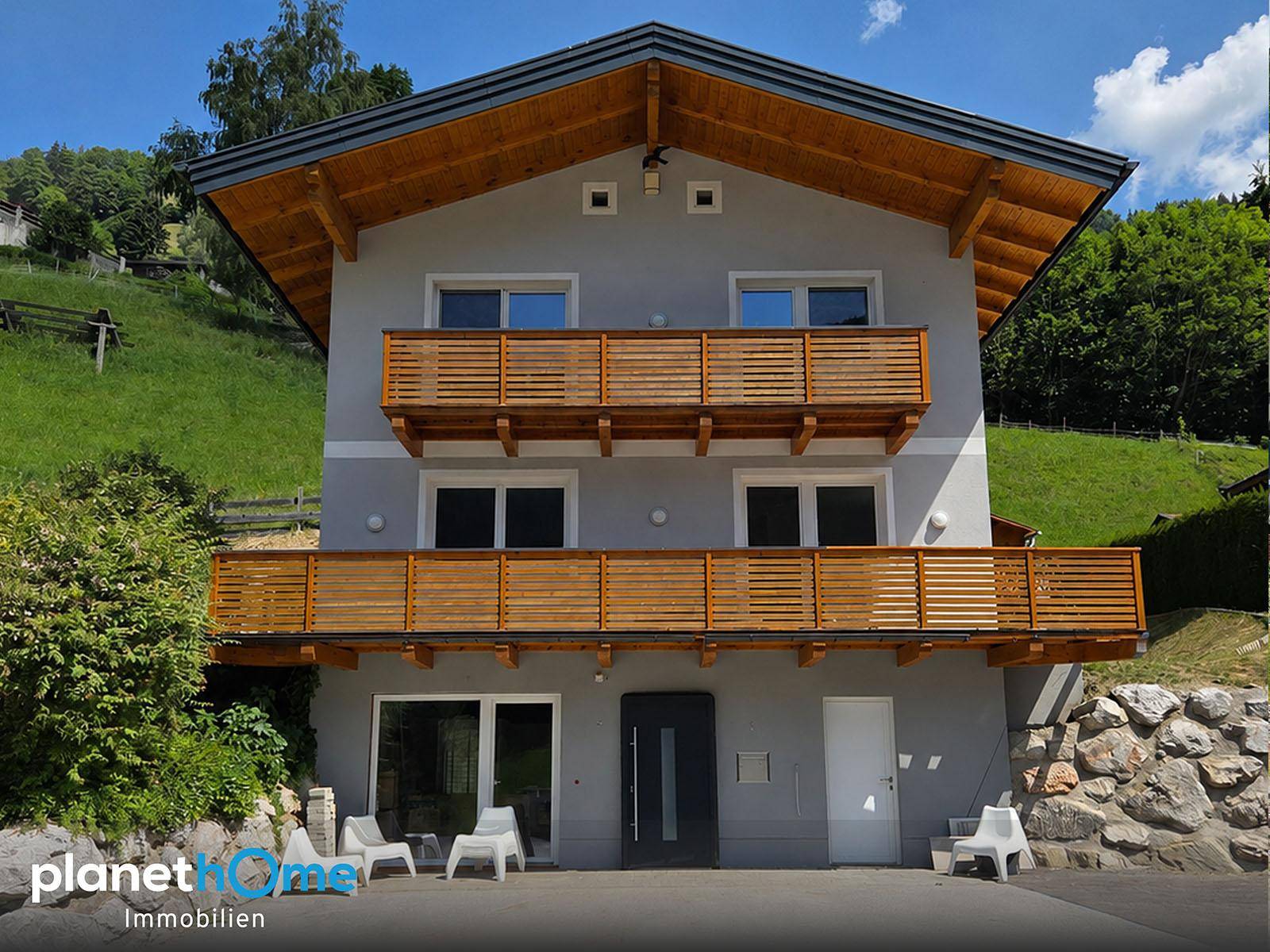 Attraktives Wohnhaus mit Holzdetails und Balkonen, umgeben von grüner Natur.