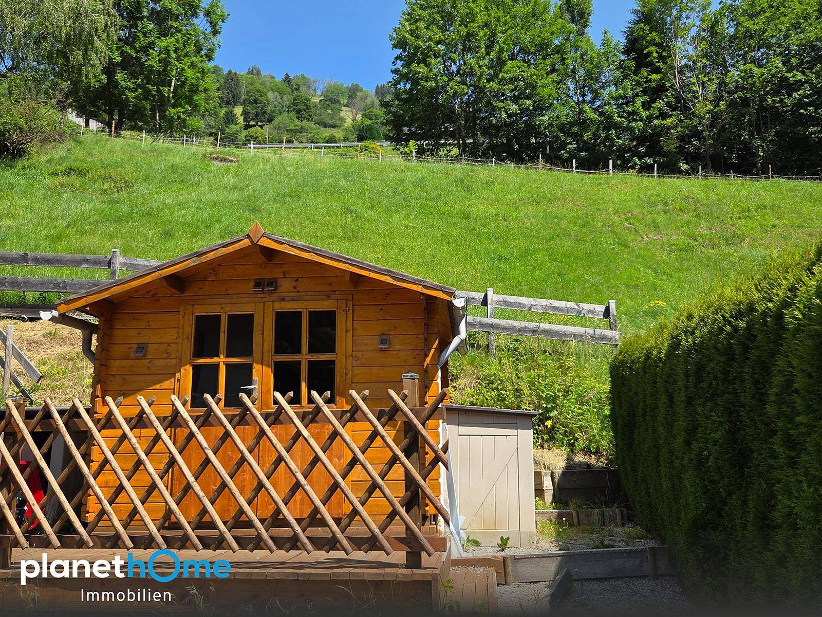 Rustikales Gartenhaus aus Holz mit kleiner Terrasse, umgeben von üppigem Grün.