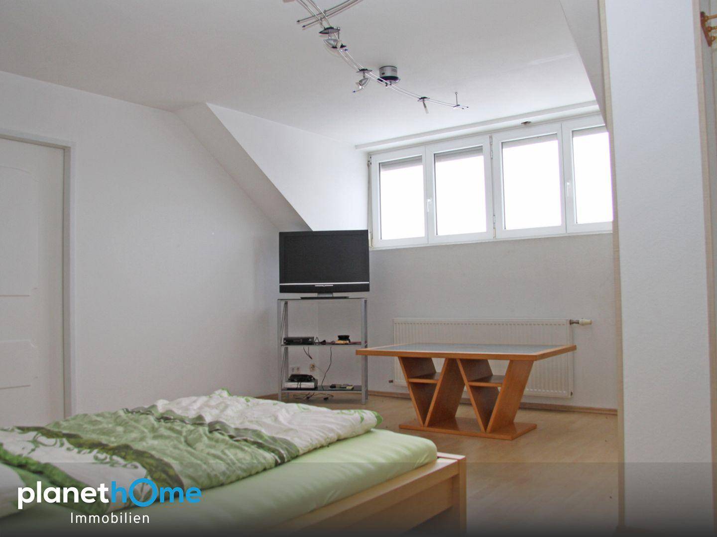 Gemütliches Schlafzimmer im Dachgeschoss mit schrägen Wänden, Fenster und hellem Holzboden.