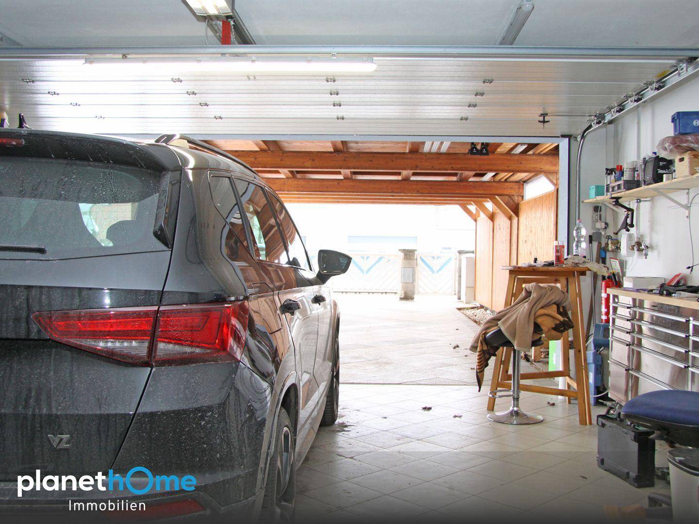 Geräumige Garage mit einem geparkten Auto, Werkbank und direktem Zugang zum Außenbereich.
