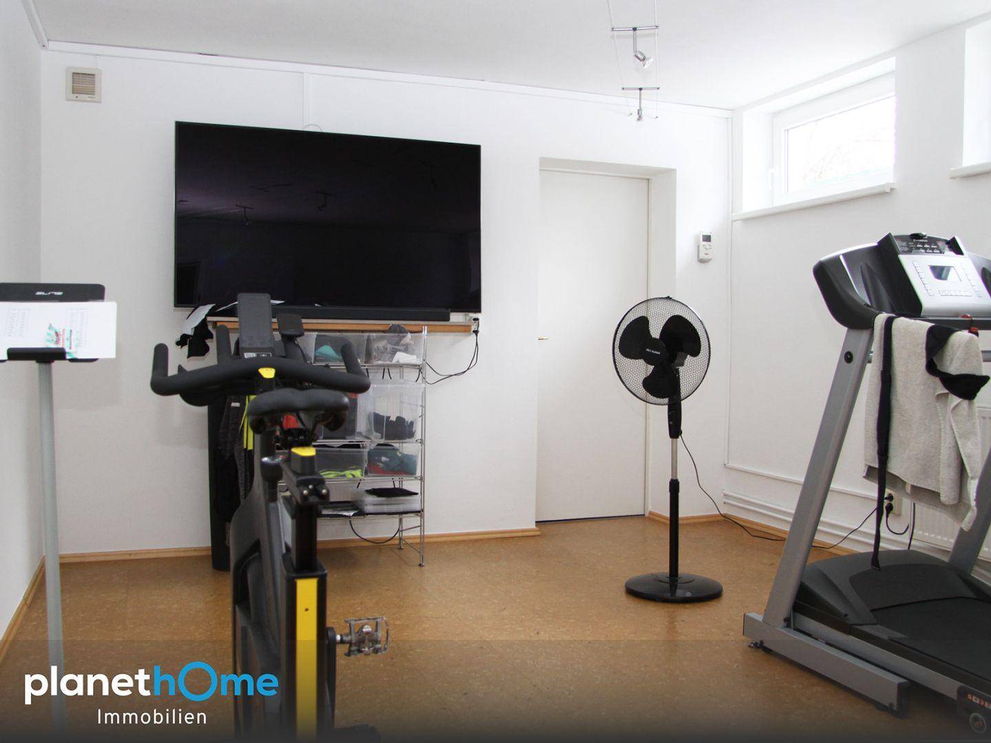 Gut ausgestatteter Fitnessraum mit Laufband, Heimtrainer und großem Fernseher für das tägliche Training.