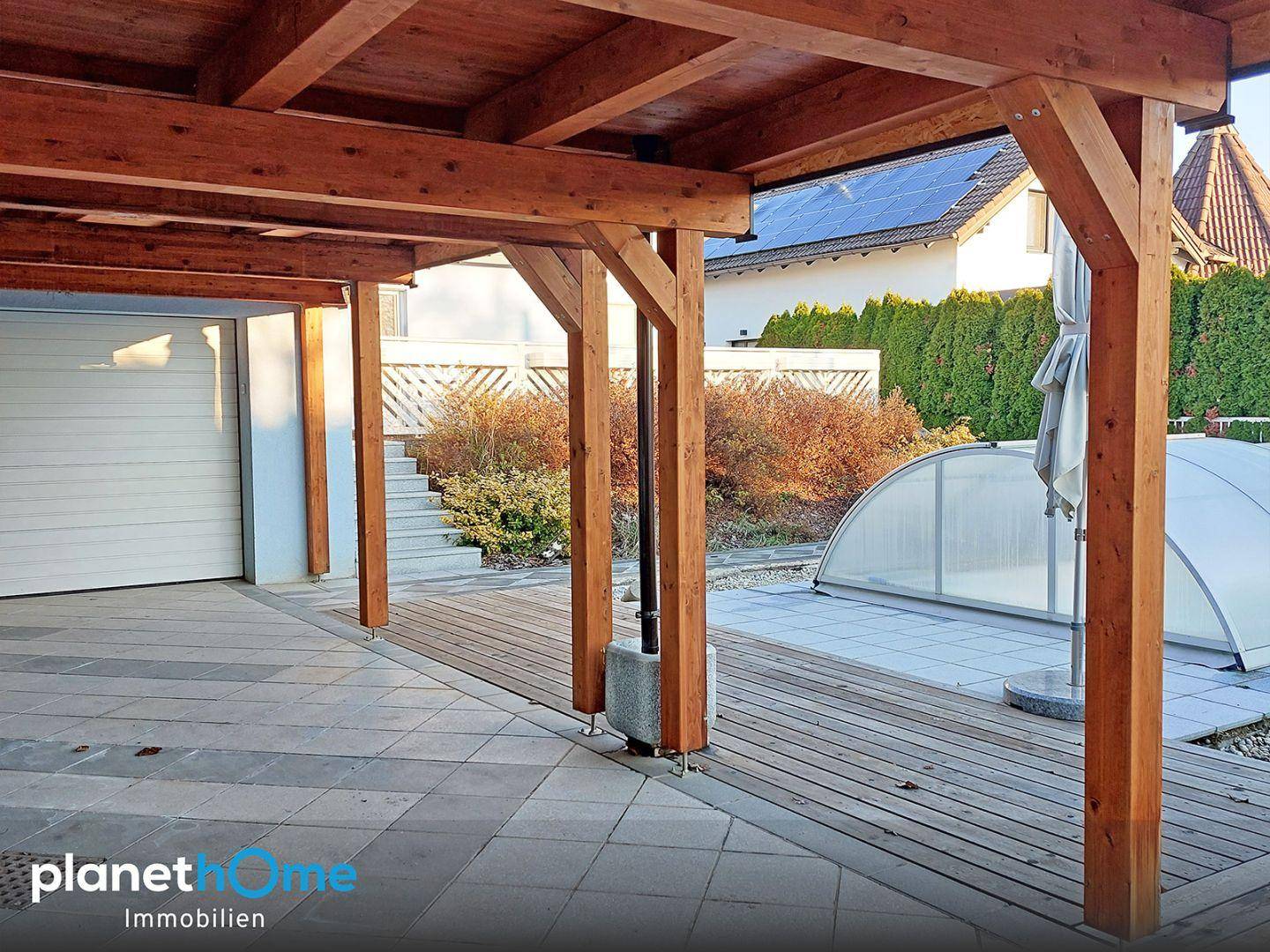 Überdachte Terrasse mit Holzbalken und Fliesenboden, angrenzend an den Poolbereich und Garten.