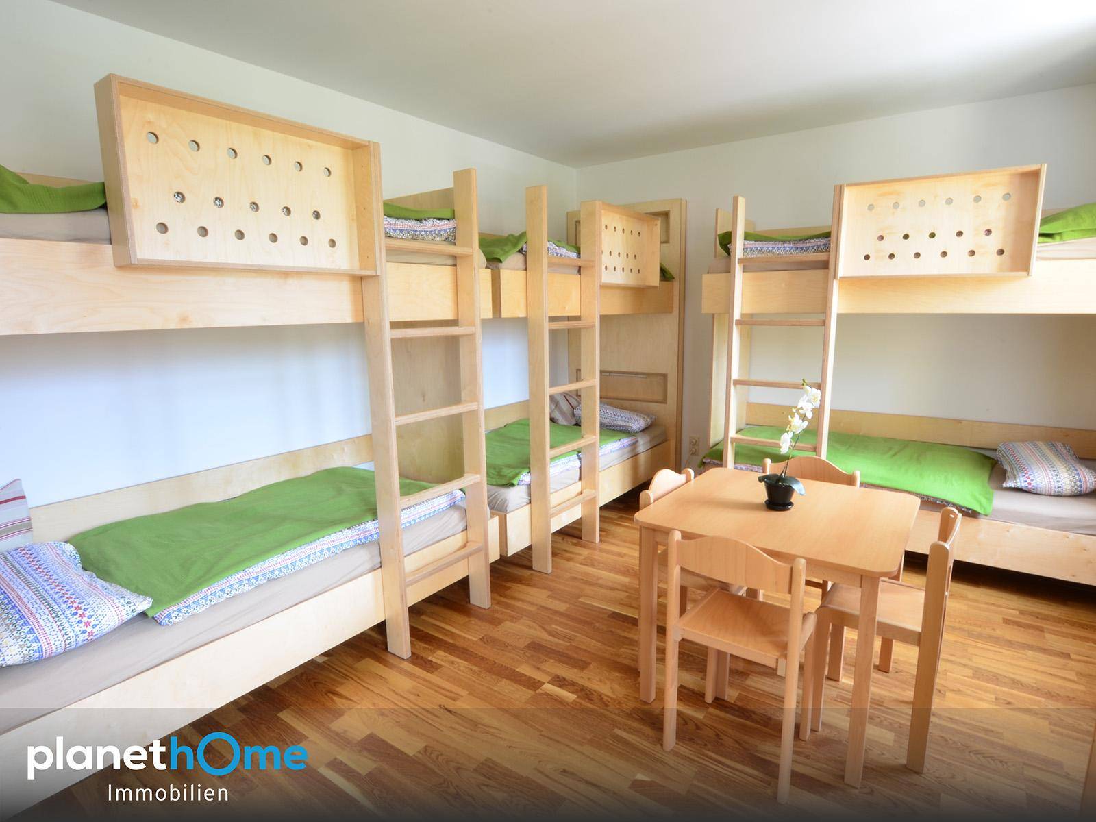 Helles Schlafzimmer mit mehreren Holz-Etagenbetten und einem kleinen Tisch in der Mitte.