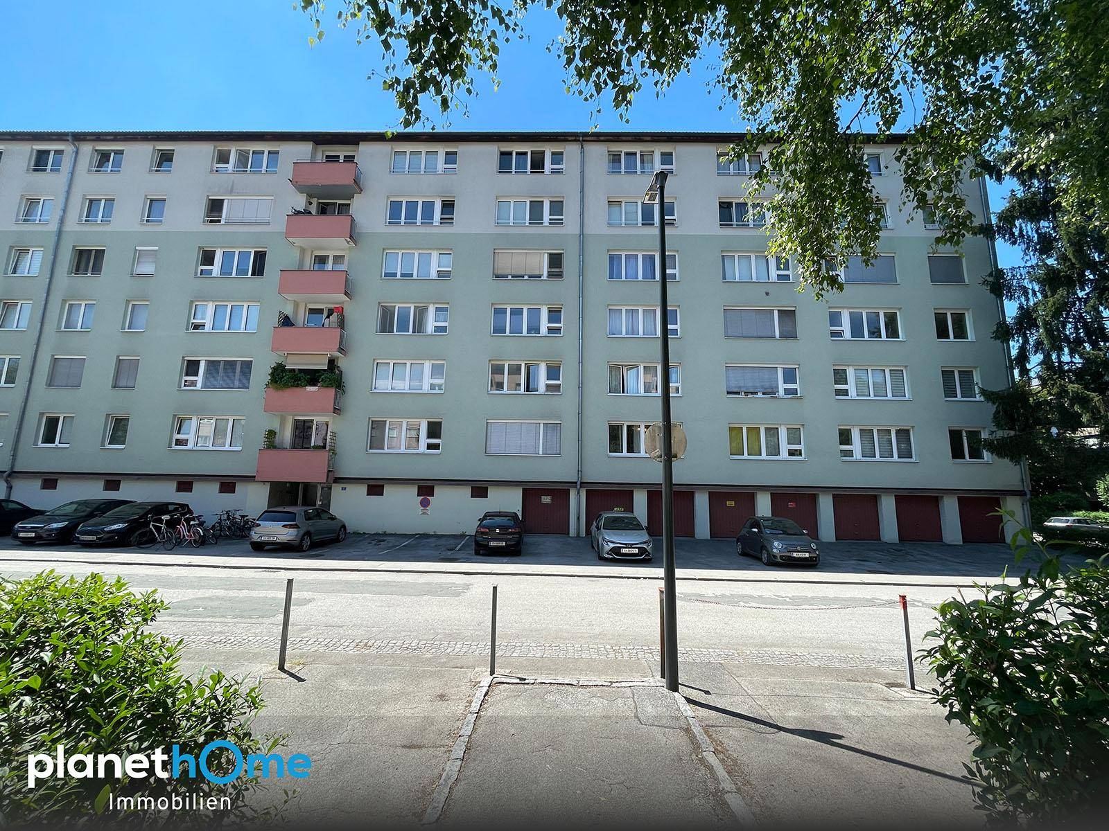 Mehrfamilienhaus mit zahlreichen Balkonen und Garagen im Erdgeschoss an einem sonnigen Tag.