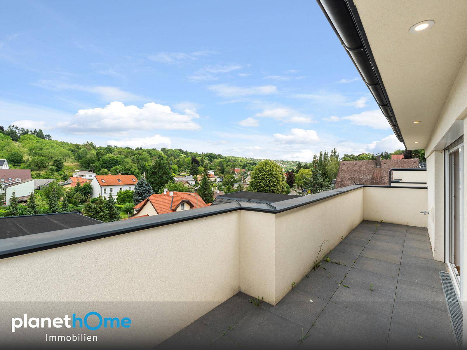 Geräumiger, leerer Balkon mit Fliesenboden und weitem Blick über die grüne Umgebung.
