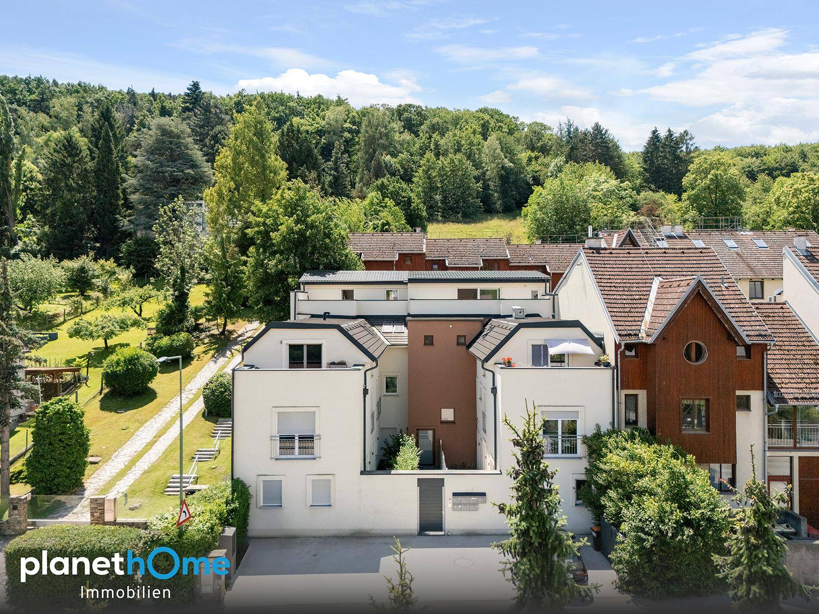Luftaufnahme eines modernen Wohnkomplexes mit mehreren Einheiten, umgeben von viel Grün.