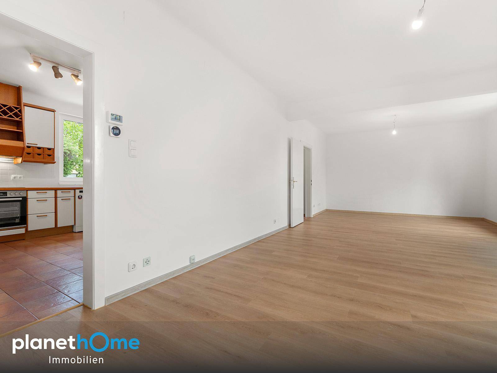 Geräumiges Wohnzimmer mit Laminatboden und Zugang zu einer gefliesten Küche.