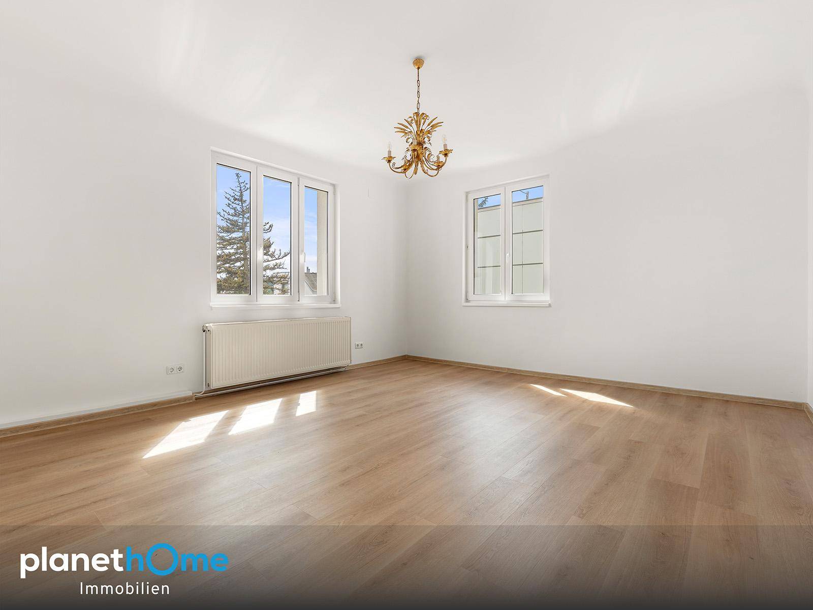 Geräumiges Schlafzimmer mit Laminatboden, zwei Fenstern und einem dekorativen Kronleuchter.