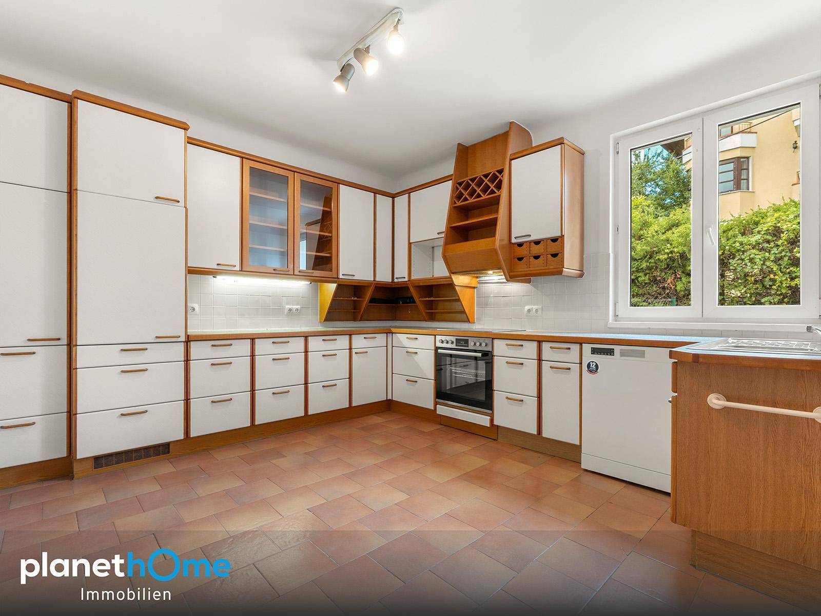 Traditionelle Küche mit weißen Schränken, Holzdetails, Fliesenboden und Fensterblick.