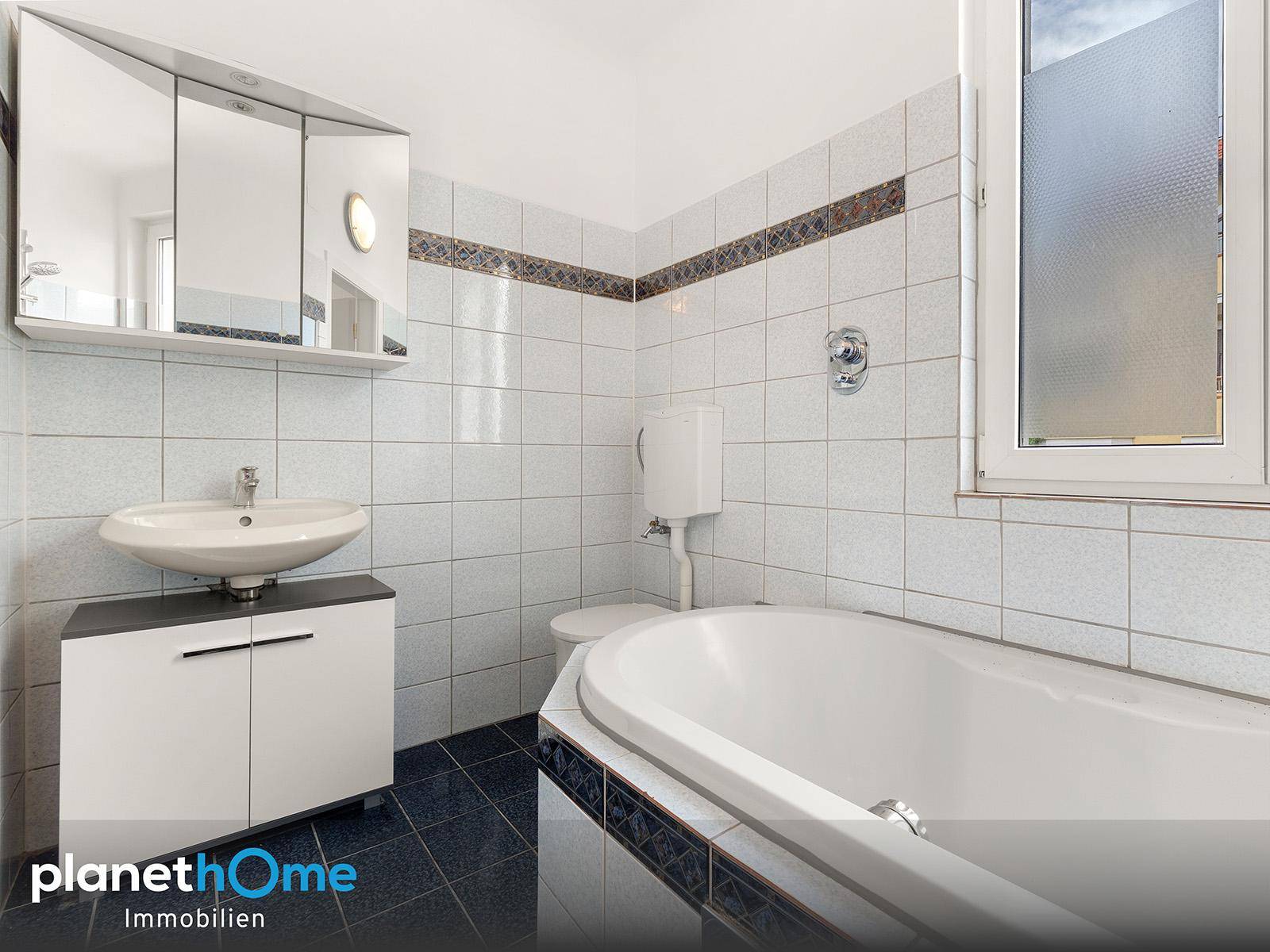 Badezimmer mit Badewanne, Waschbecken, WC und hellblauen Fliesen im 80er-Jahre-Stil.
