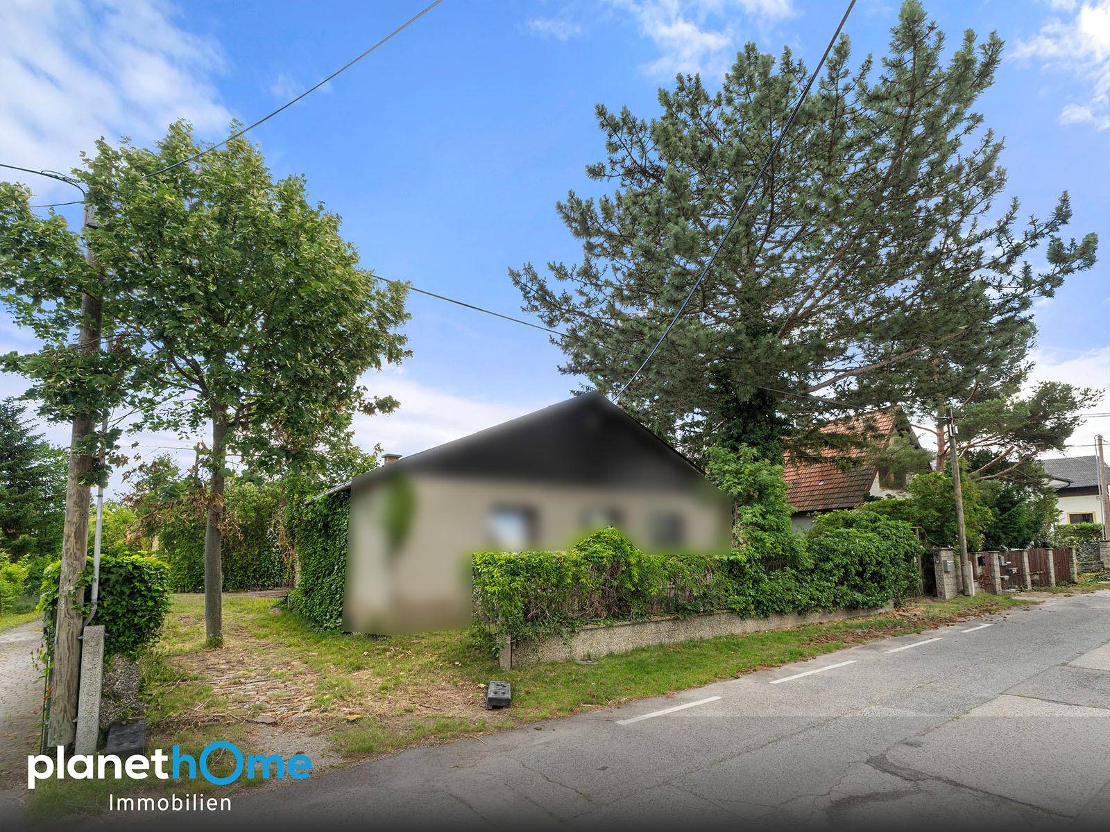Hausansicht von der Straße mit Bäumen und einer Hecke, die das Gebäude teilweise verdeckt.