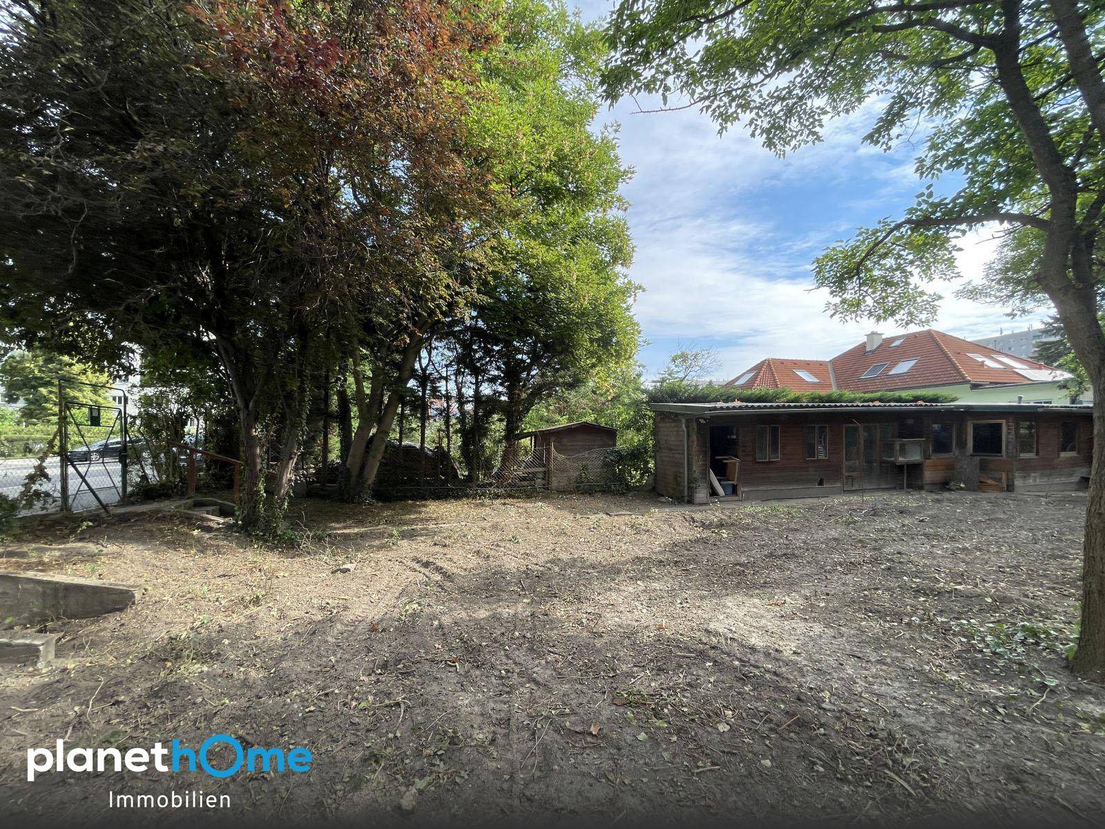 Holzgebäude mit einfacher Bauweise und großem Gartenbereich, umgeben von Bäumen und Sträuchern.