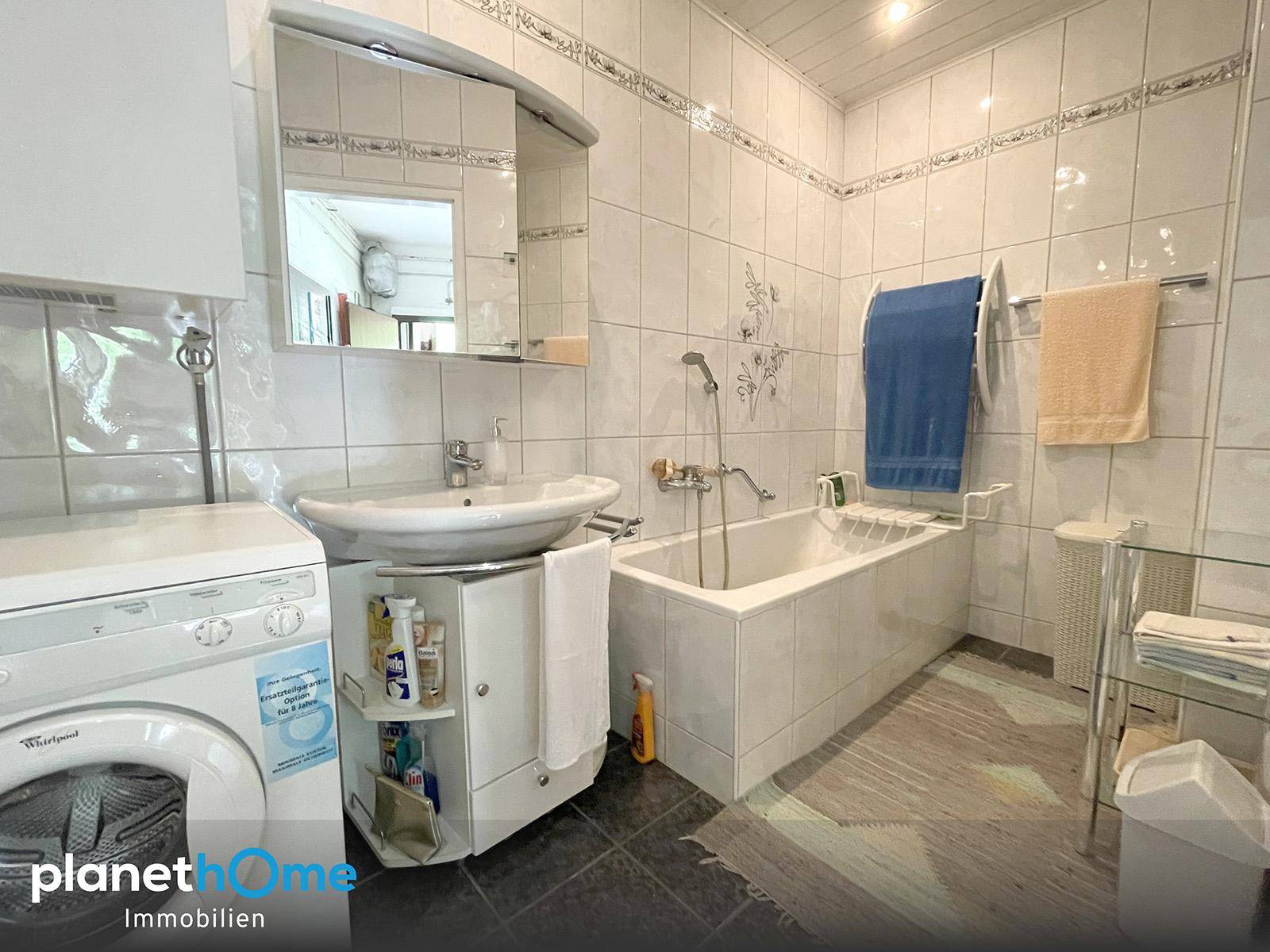Gefliestes Badezimmer mit Badewanne, Waschbecken und Waschmaschine.