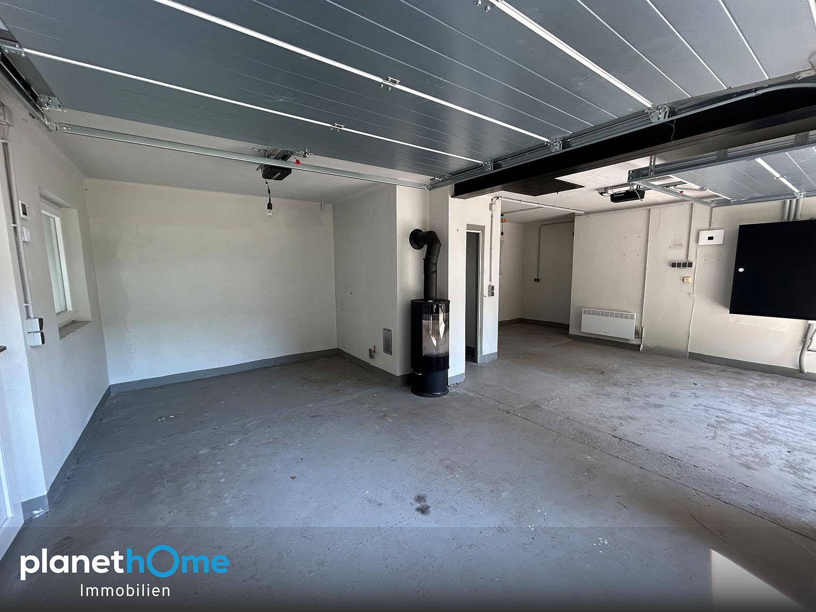 Geräumige Garage mit Betonboden, Holzofen und Rolltoren, bereit zur Nutzung.
