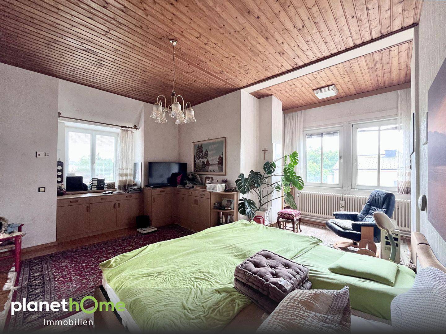 Gemütliches Schlafzimmer mit Holzdecke, Teppichboden und großen Fenstern für viel Tageslicht.