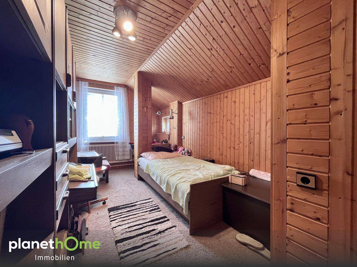 Gemütliches Schlafzimmer im Dachgeschoss mit Holzverkleidung an Wänden und Decke sowie Dachschräge.