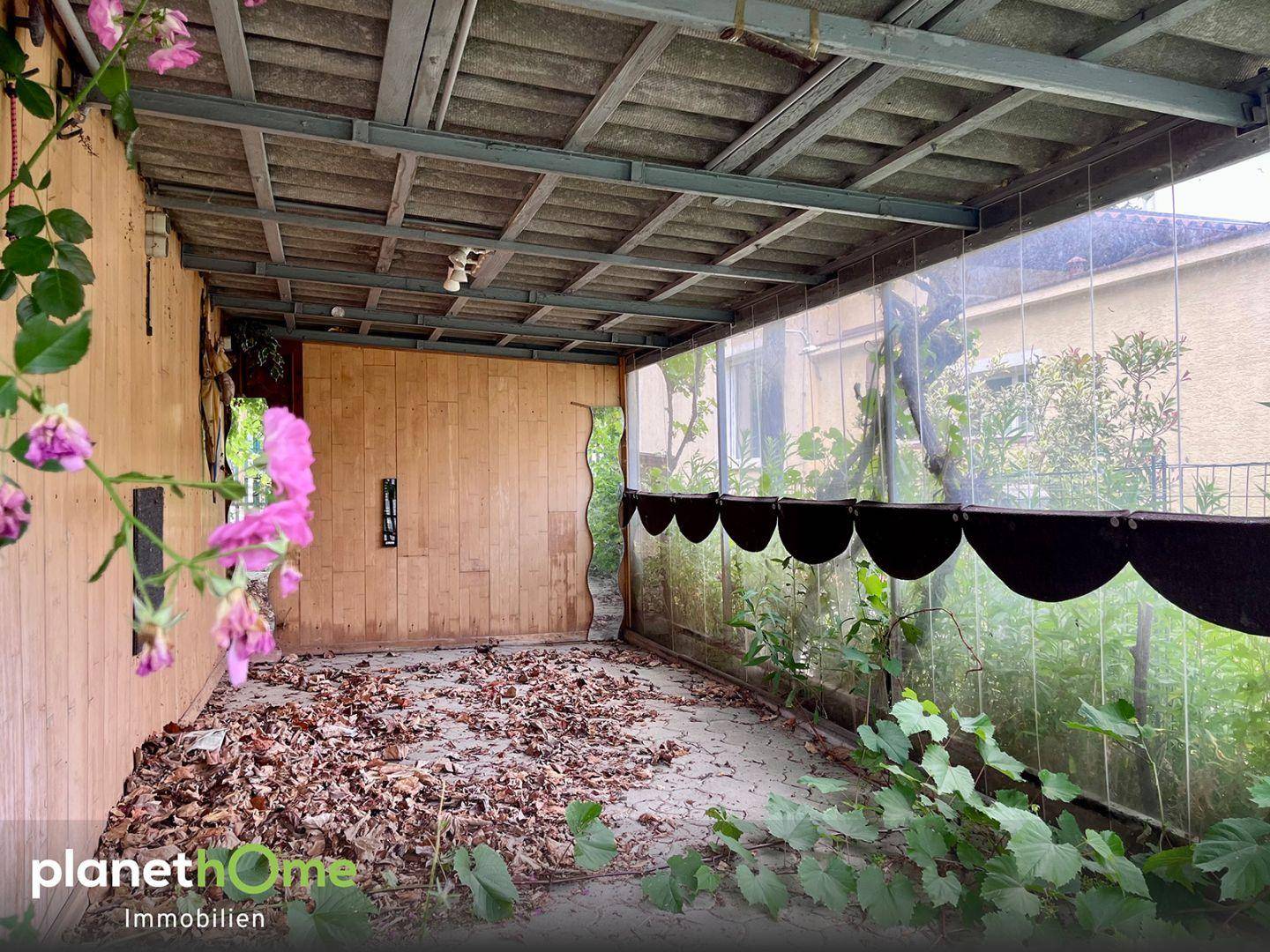 Überdachter Außenbereich, möglicherweise eine Loggia, mit Holzwand und Blick ins Grüne.