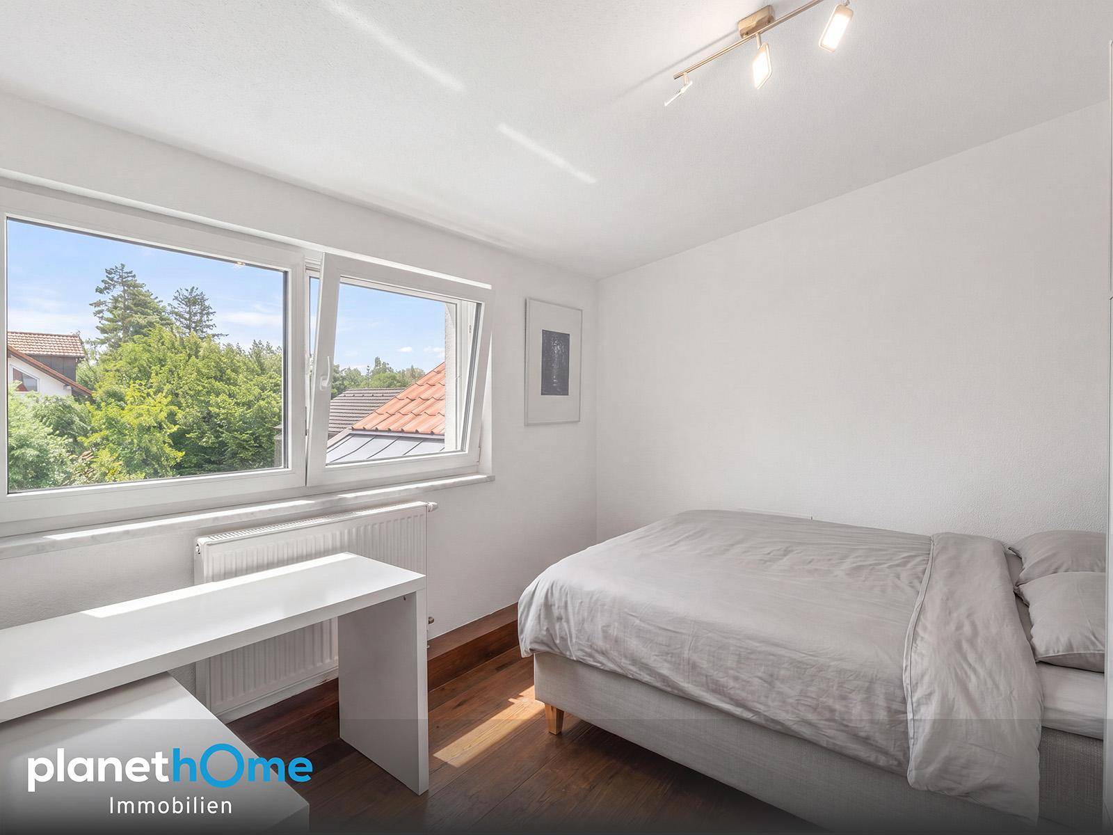 Helles Schlafzimmer mit Holzboden, großem Fenster und Blick ins Grüne.