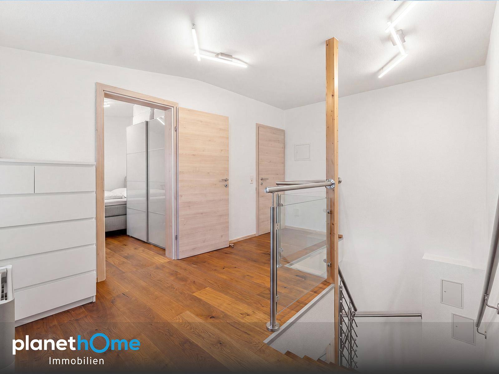 Heller Flur im Obergeschoss mit Holzparkett und moderner Treppe zum nächsten Stockwerk.