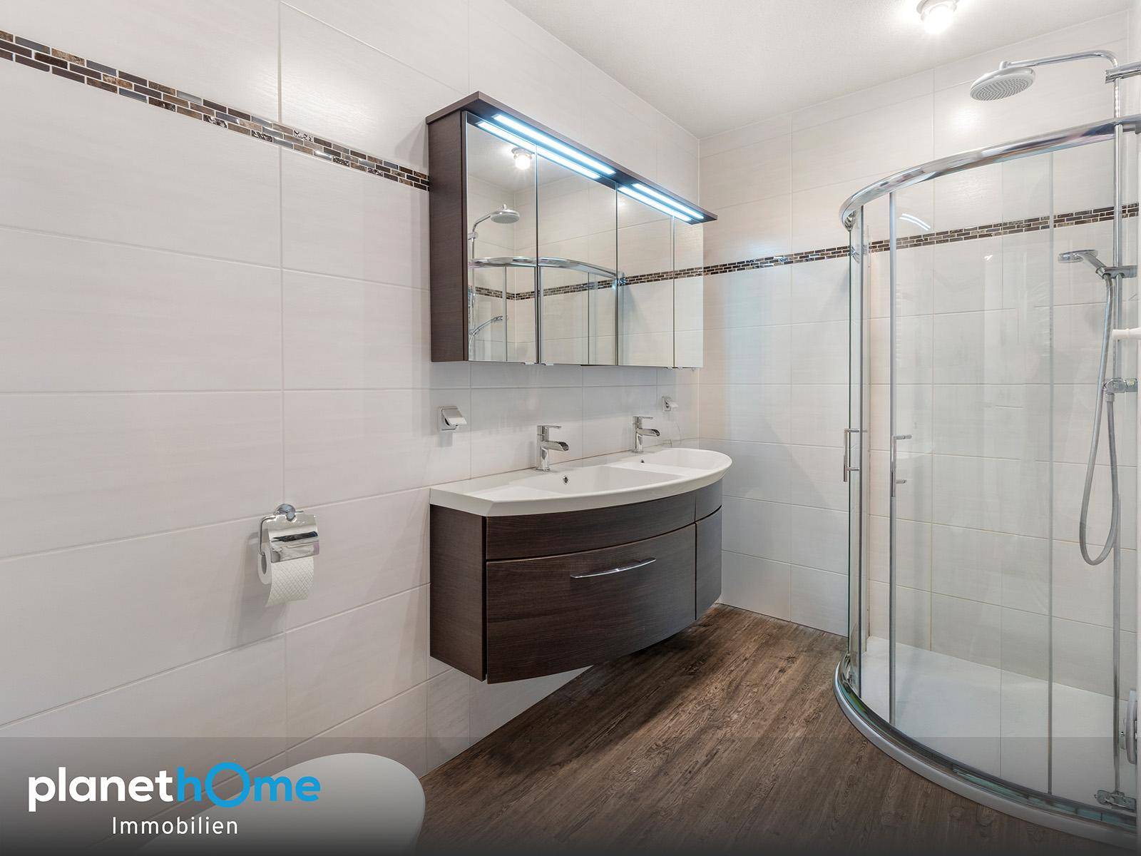 Modernes Badezimmer mit Doppelwaschbecken, Duschkabine und hellen Fliesen.