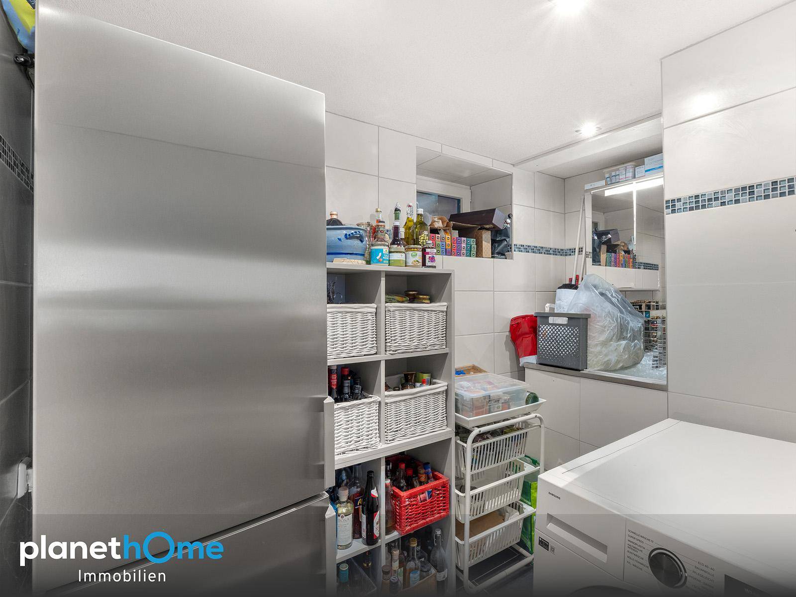 Praktischer Hauswirtschaftsraum mit Waschmaschine, Kühlschrank und Regalen für Vorräte.