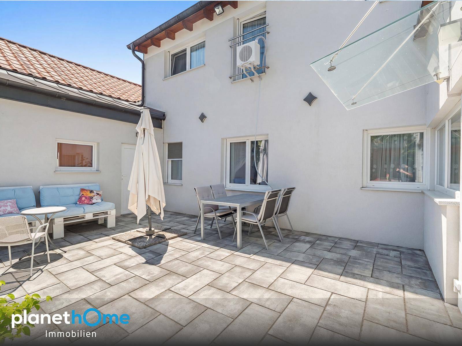 Gepflasterte Terrasse mit Sitzgelegenheiten und Sonnenschirm vor dem Haus.