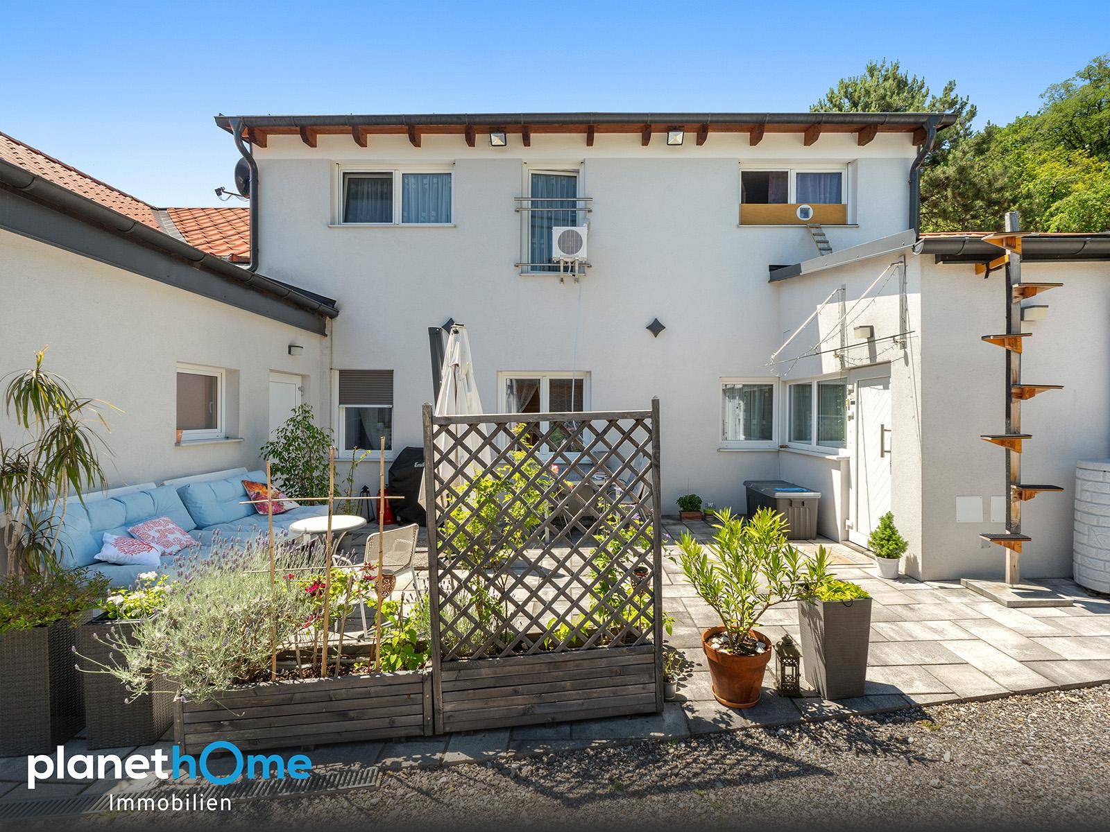 Rückseite des Hauses mit großer Terrasse, Sitzgelegenheiten und dekorativen Pflanzen.