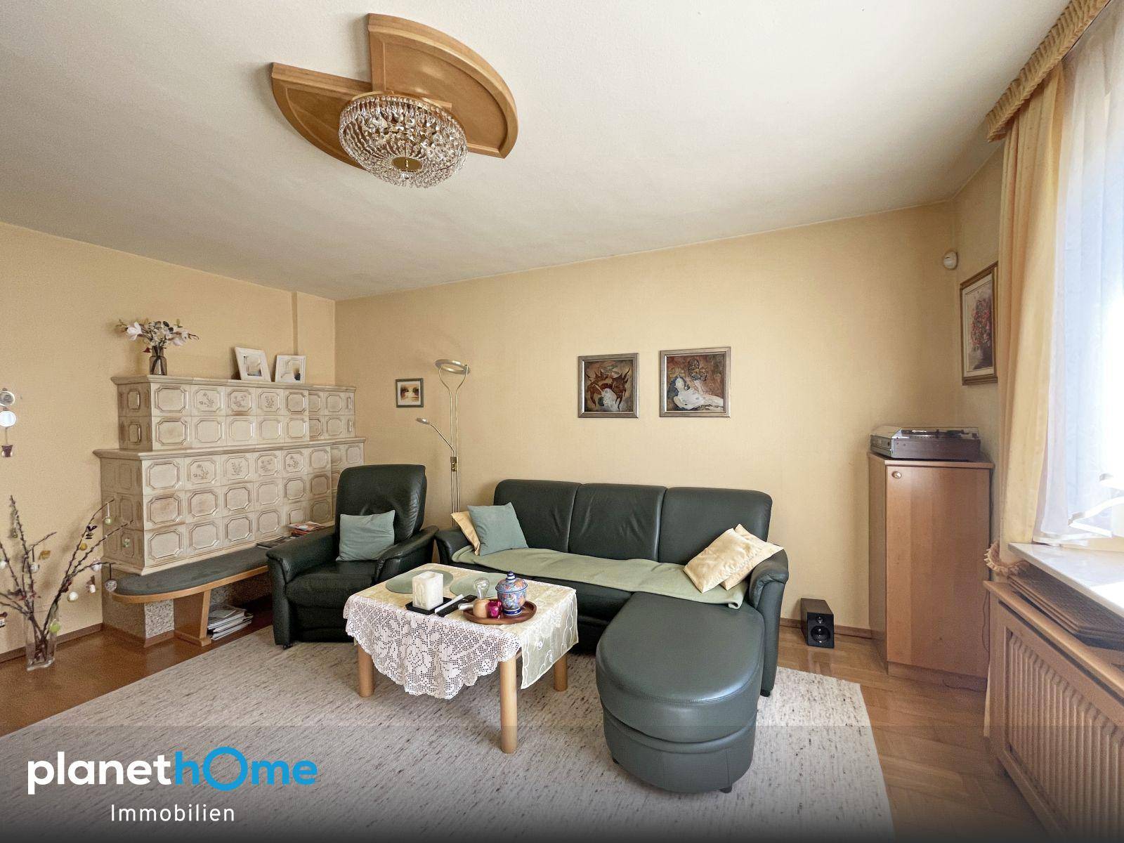 Gemütliches Wohnzimmer mit Kachelofen, Ledersofa und Parkettboden, hell und einladend.