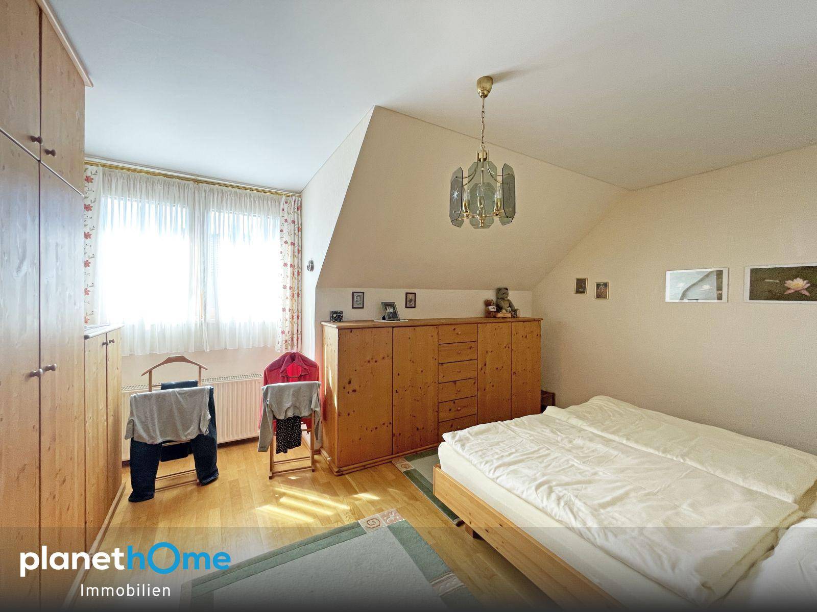 Schlafzimmer mit Holzmöbeln, Dachschräge und Teppichboden, hell und funktional eingerichtet.