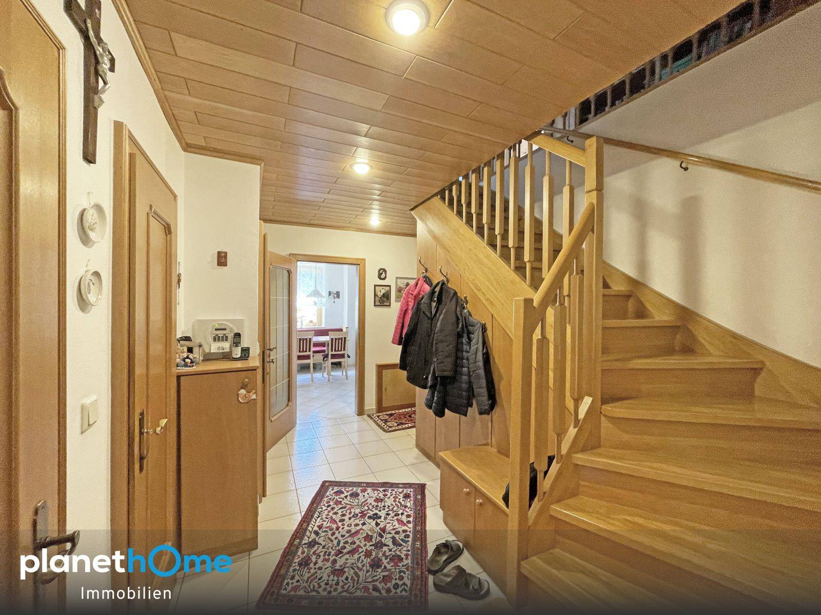 Eingangsbereich mit Holztreppe, Fliesenboden und Garderobe, hell und einladend gestaltet.