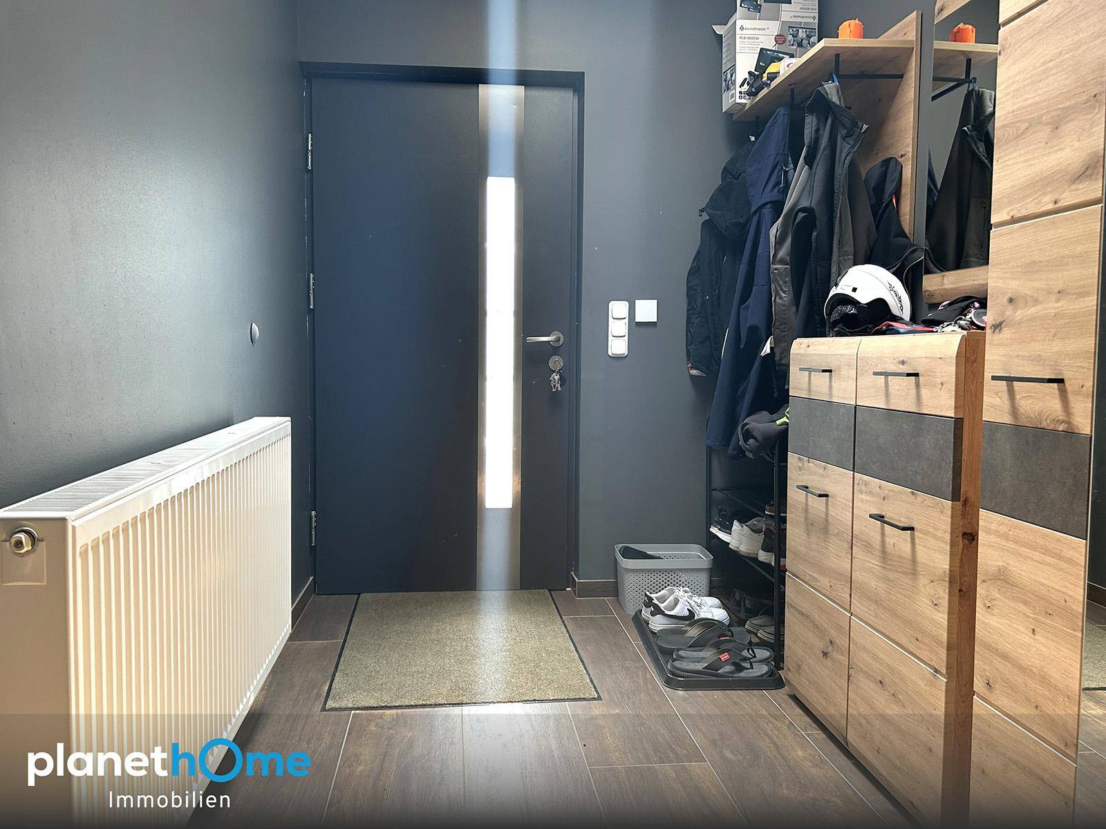 Eingangsbereich mit dunkler Tür, Heizkörper und praktischem Holzschrank für Garderobe und Schuhe.