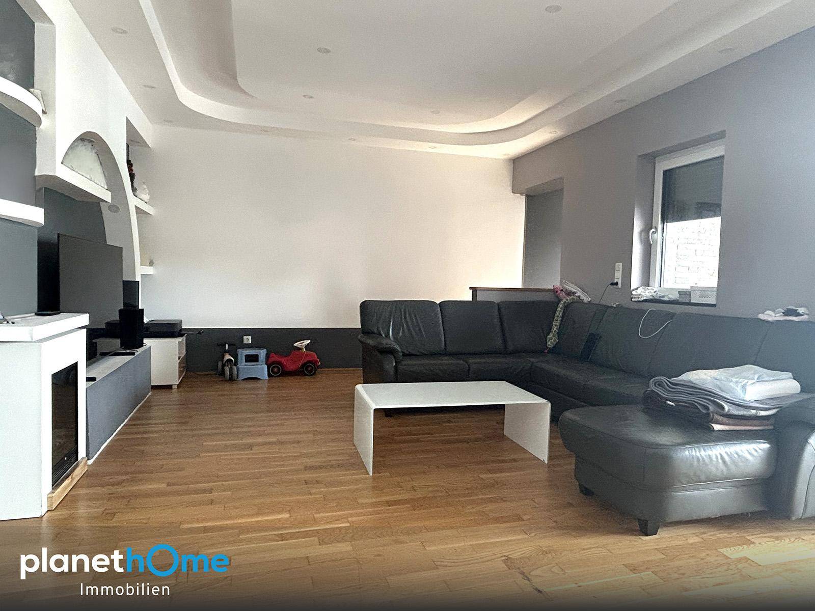 Geräumiges Wohnzimmer mit dunklem Ledersofa, Holzboden und einer modernen, geschwungenen Deckenkonstruktion.