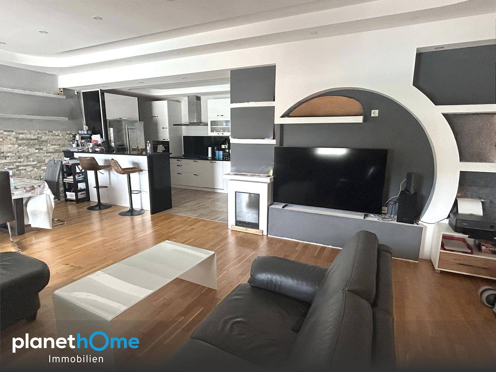 Offener Wohnbereich mit Holzboden, moderner Küche und großem Sofa, ideal für geselliges Beisammensein.