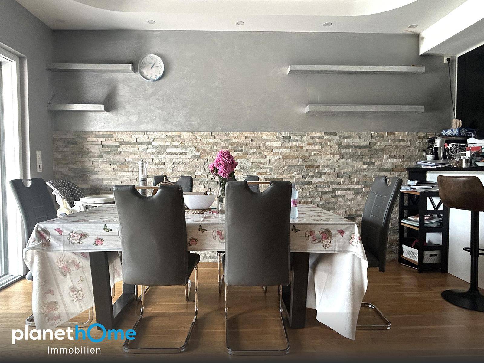 Essbereich mit großem Tisch, bequemen Stühlen und einer dekorativen Steinwand, ideal für Mahlzeiten.