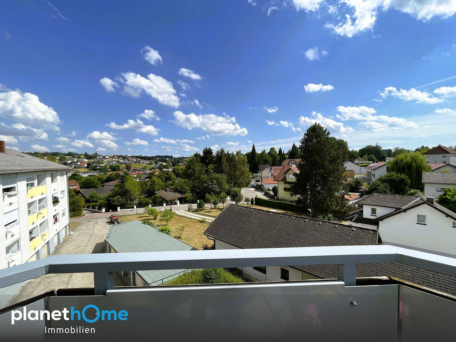 Weitblick vom Balkon über die Dächer der umliegenden Häuser und grüne Baumlandschaft.