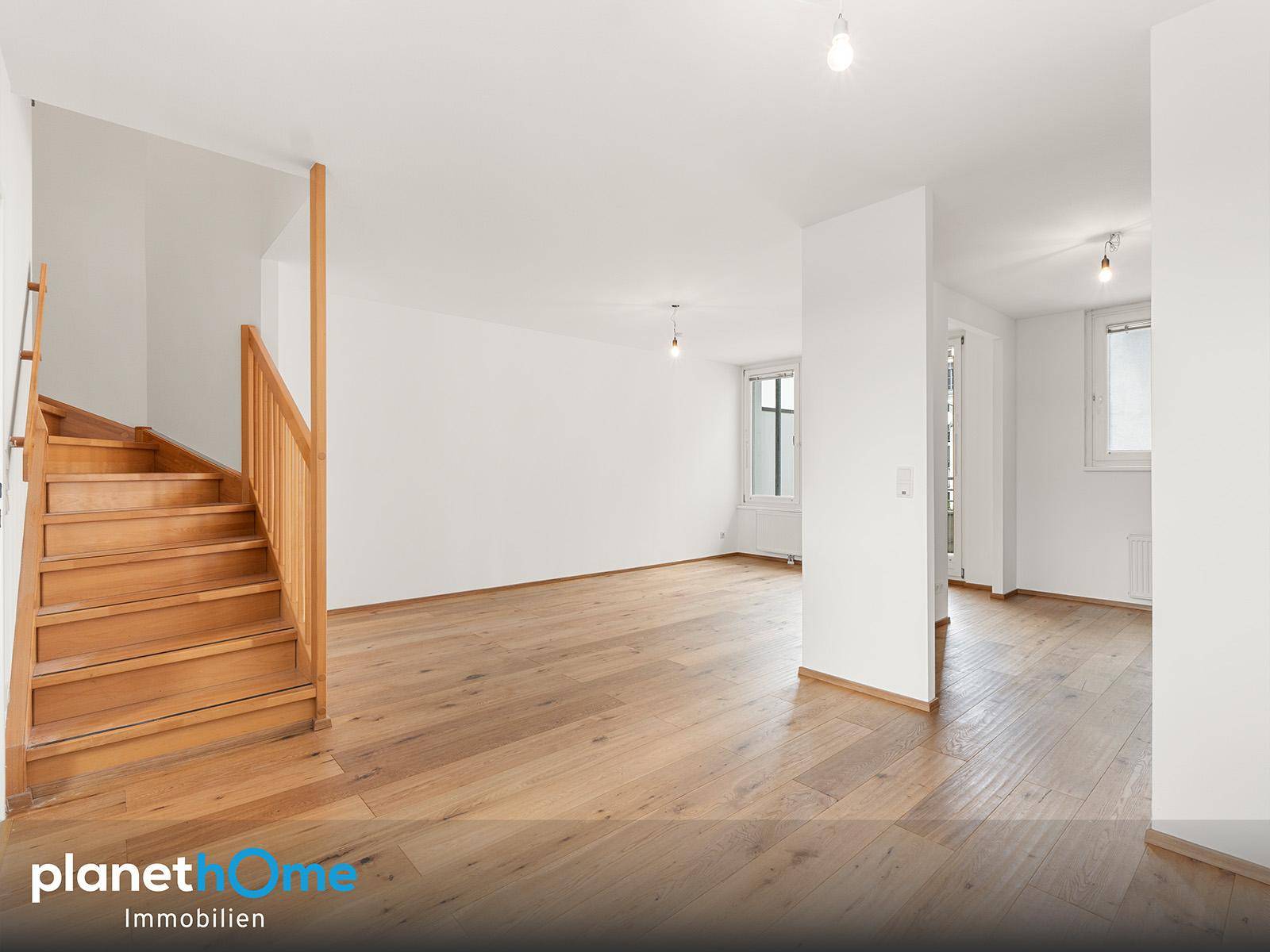 Geräumiger Wohnbereich mit hellem Holzboden und eleganter Holztreppe zum Obergeschoss.