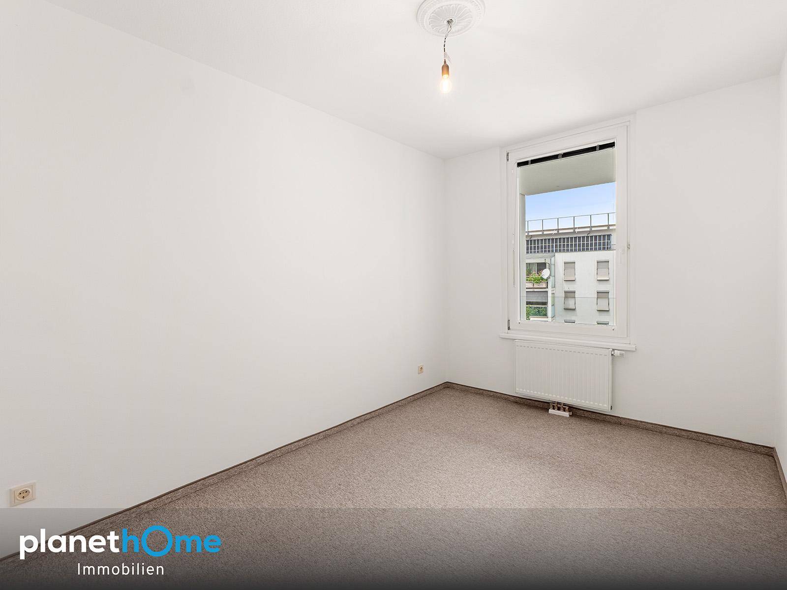 Helles Schlafzimmer mit Teppichboden und einem Fenster, das Tageslicht hereinlässt.