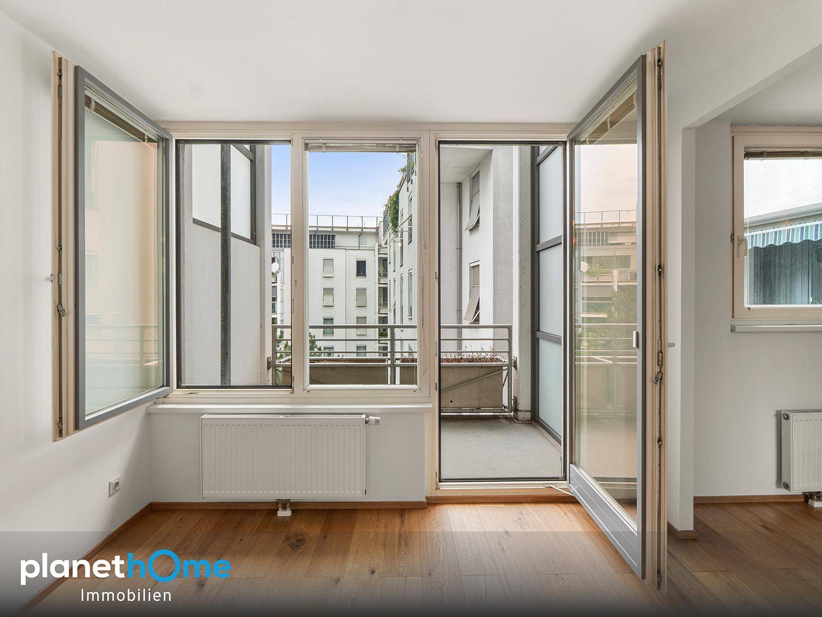 Heller Raum mit großen Fenstern und Zugang zu einem kleinen Balkon mit Stadtblick.