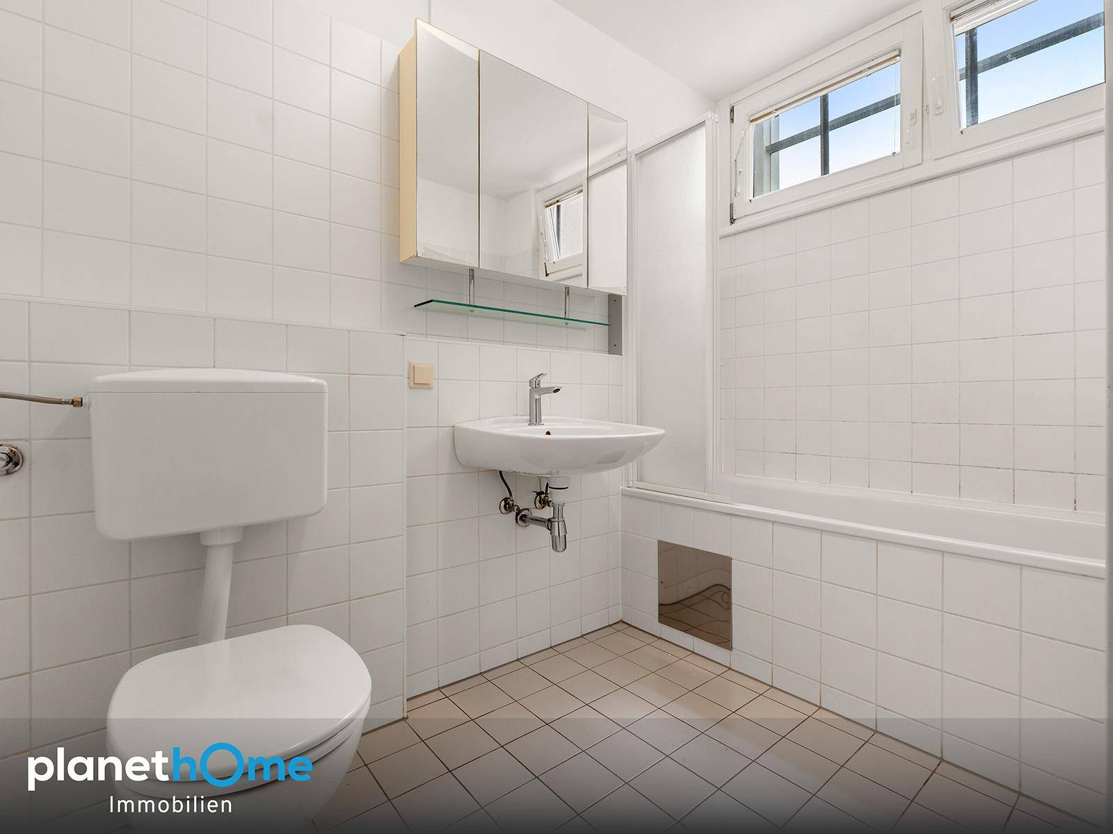 Funktionales Badezimmer mit weißen Fliesen, Badewanne, Waschbecken und Fenster.