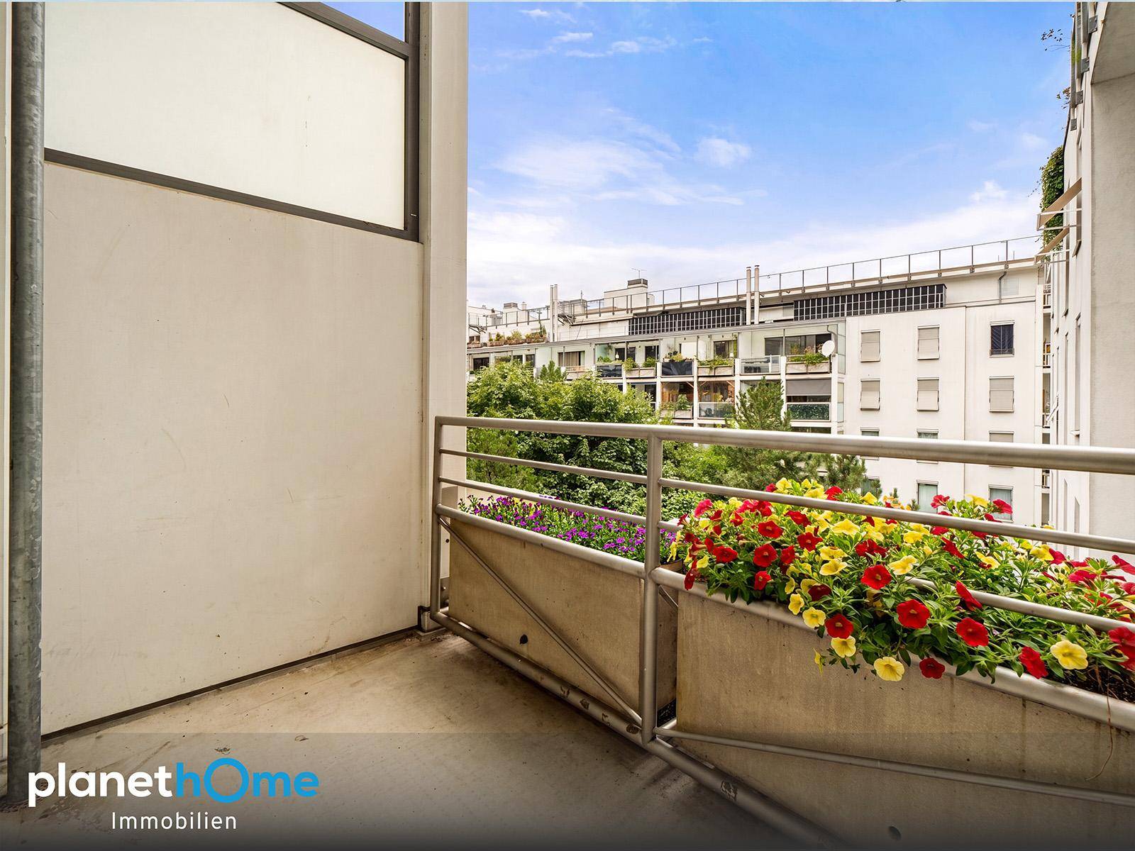 Kleiner Balkon mit bunten Blumenkästen und Blick auf die umliegenden Gebäude.