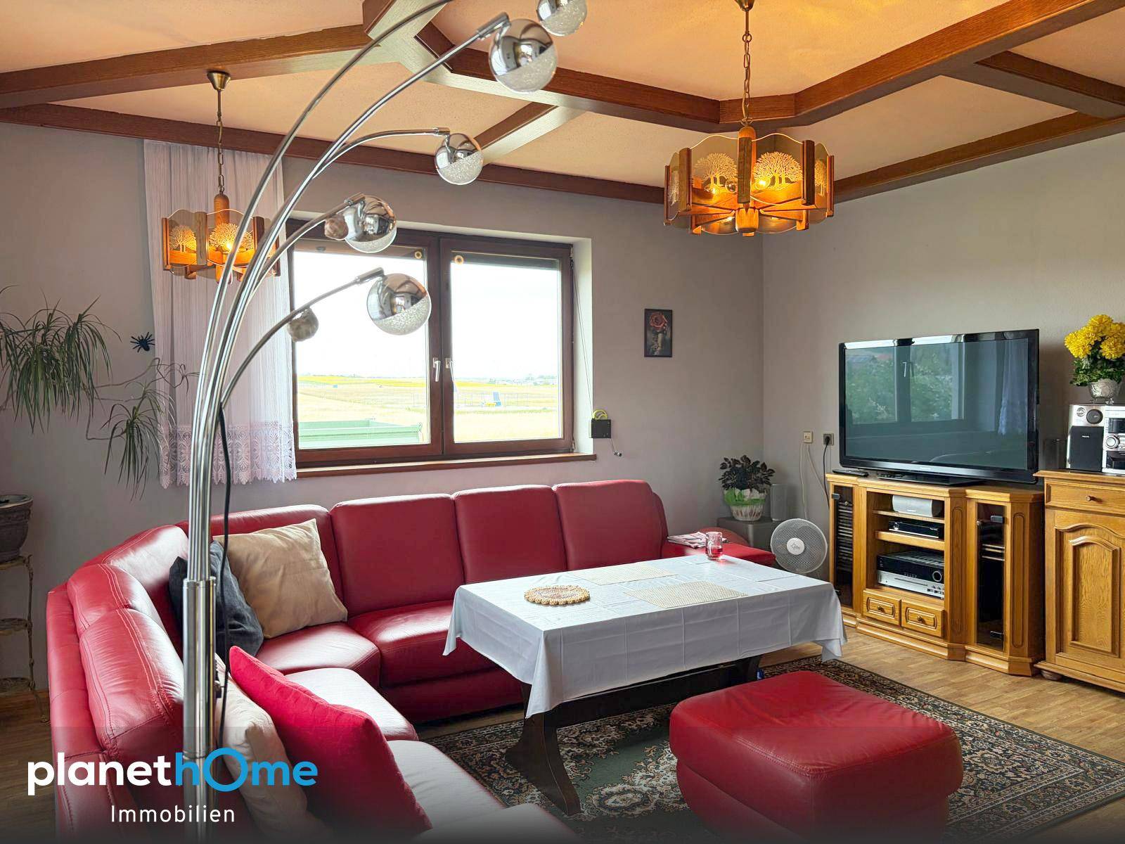 Gemütliches Wohnzimmer mit roter Ledercouch, Holzbalkendecke und traditioneller Einrichtung.