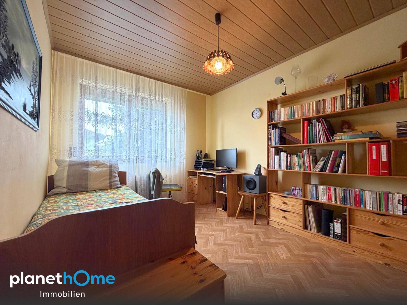 Helles Schlafzimmer mit Holzdecke, Einzelbett, Bücherregal und Blick ins Grüne.