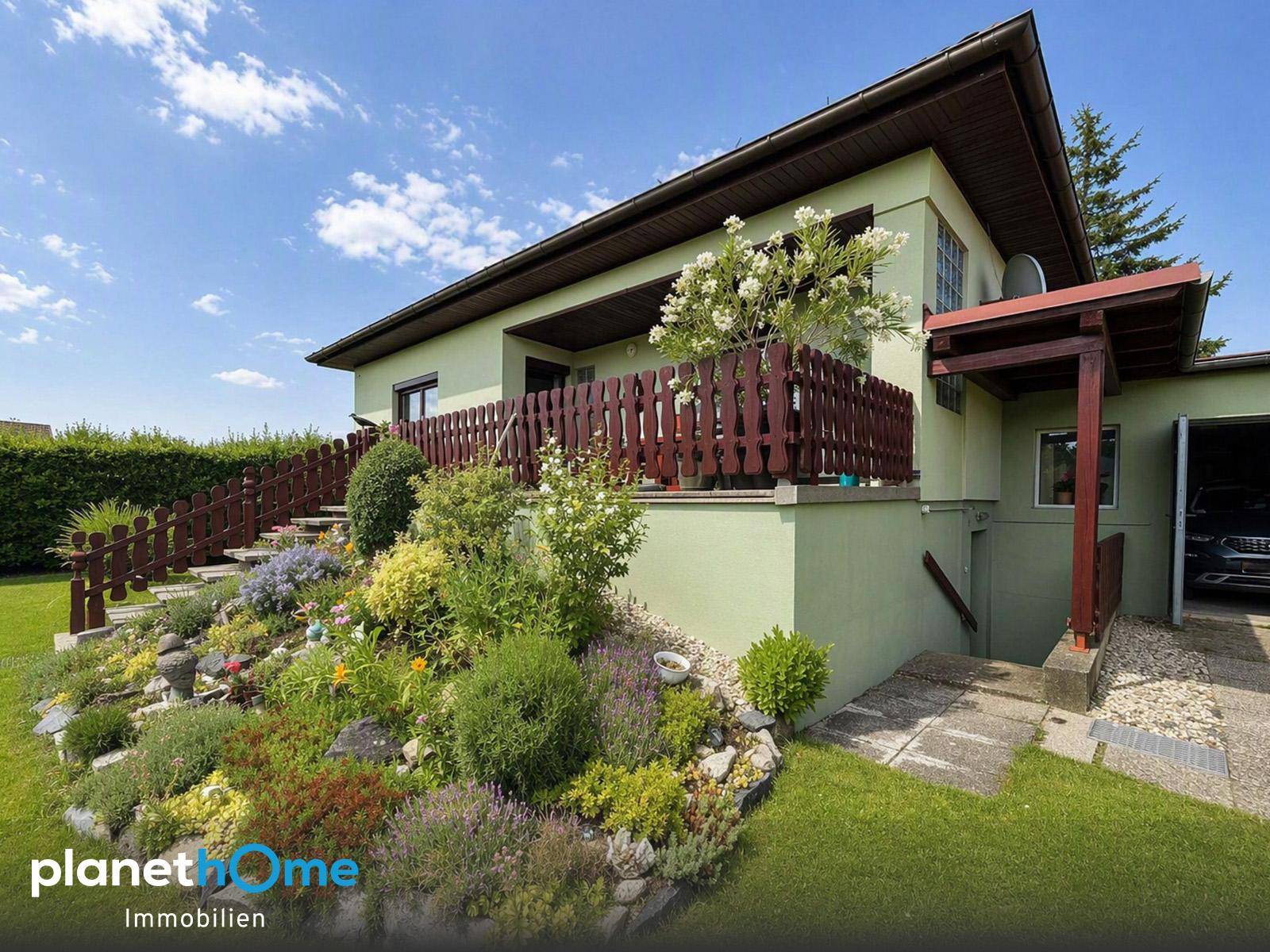 Seitlicher Blick auf das Haus mit terrassiertem Garten, üppiger Bepflanzung und Garagenzufahrt.