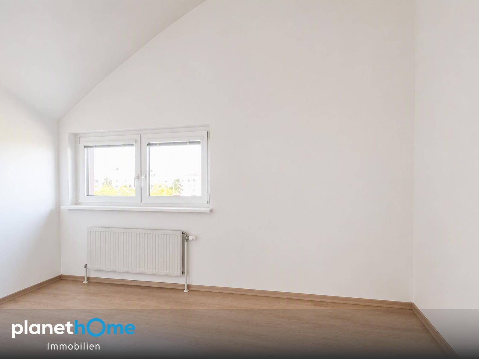 Leeres Schlafzimmer mit Laminatboden, Fenster und Dachschräge.