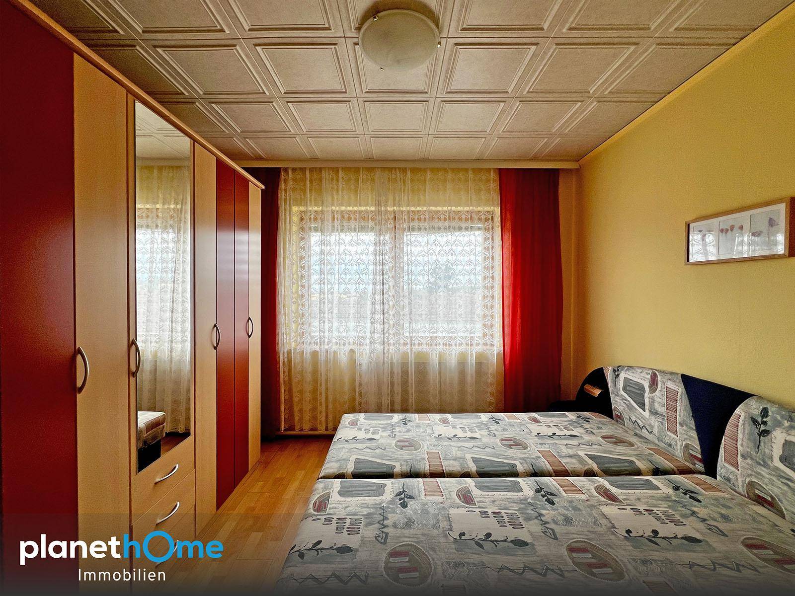 Schlafzimmer mit zwei Einzelbetten, Spiegelschrank und gemusterter Decke, hell durch das Fenster.