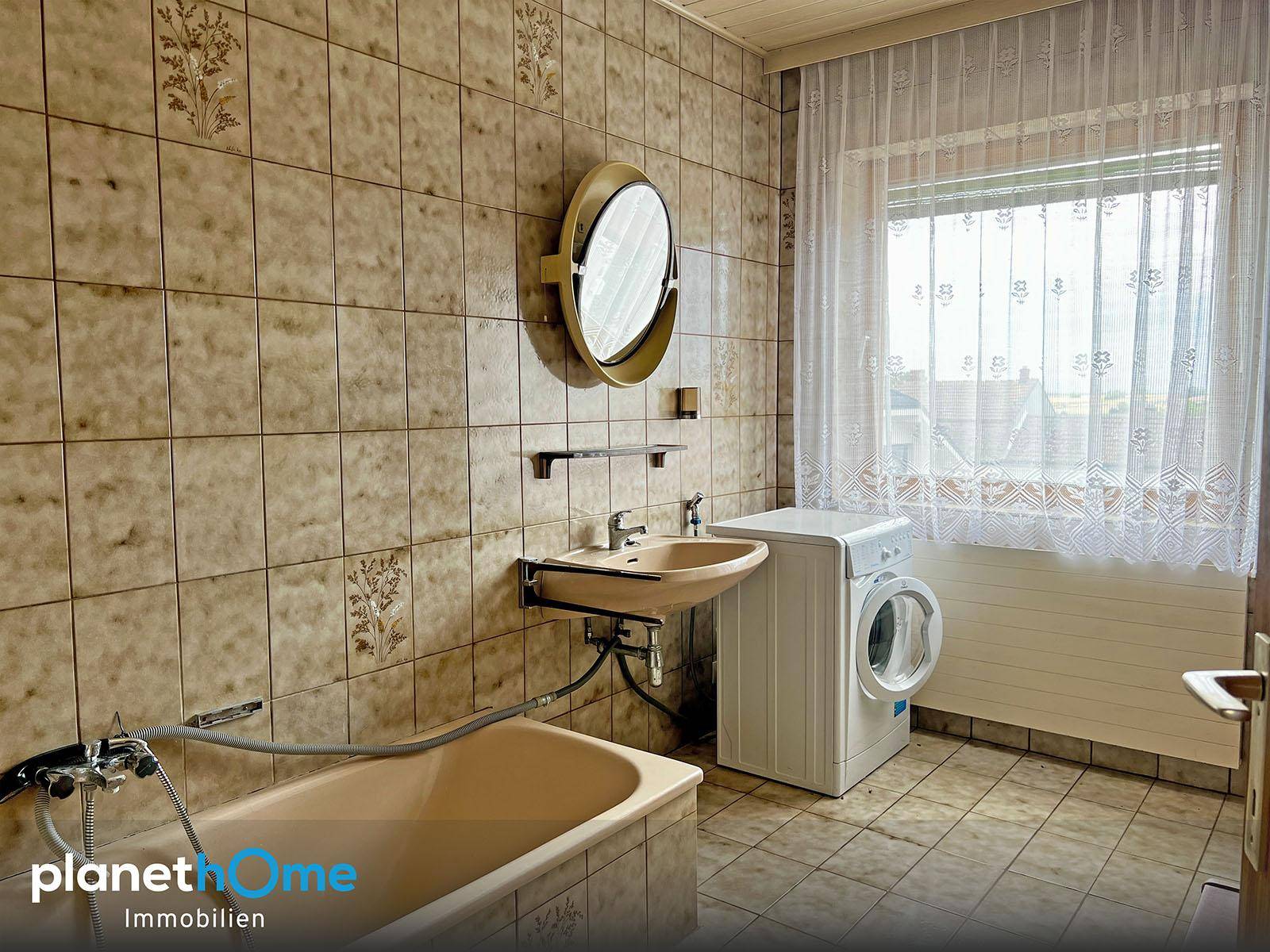 Badezimmer im 80er-Jahre-Stil mit Badewanne, Waschbecken und Waschmaschine, hell durch das Fenster.